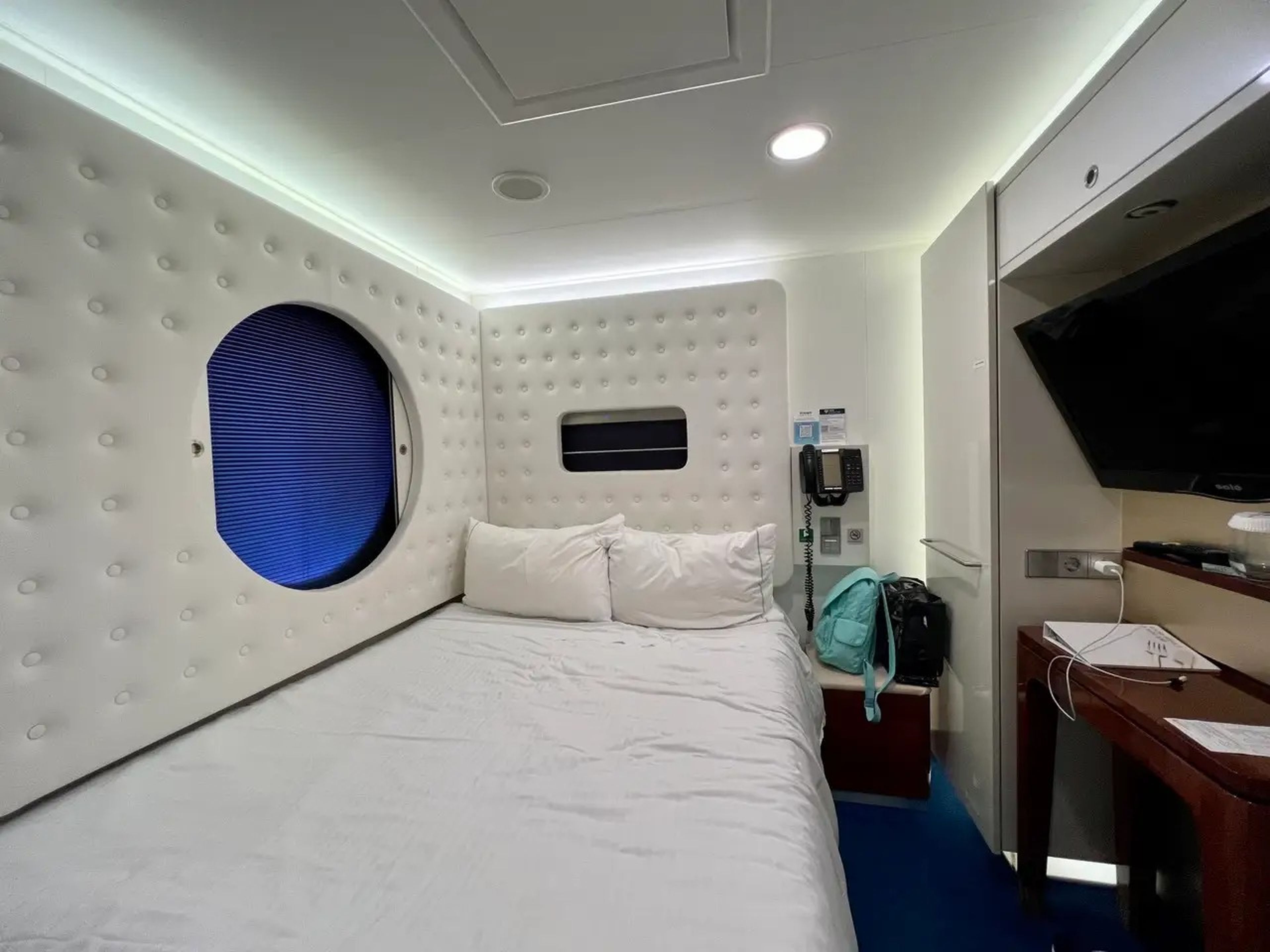 Studio stateroom on the NCL Getaway with a window into the hallway and white quilted walls around a bed