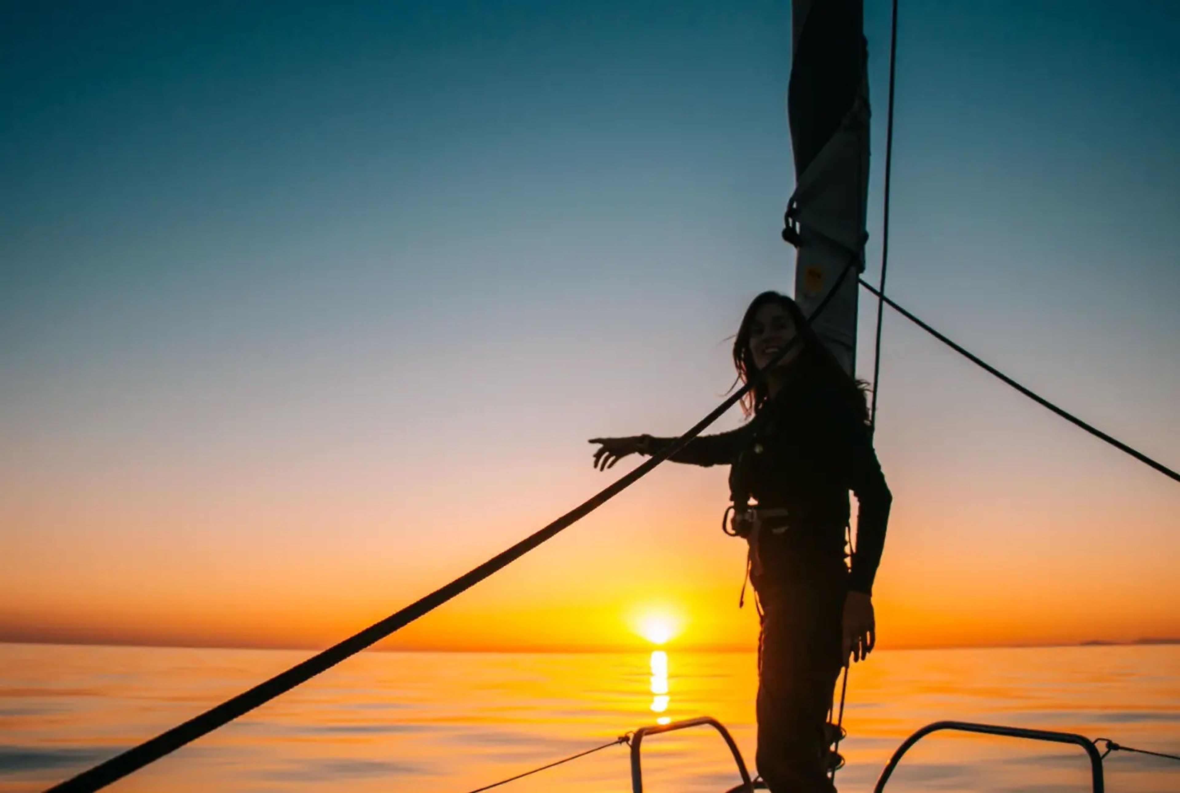 A woman pointing to the horizon on a sailboat.