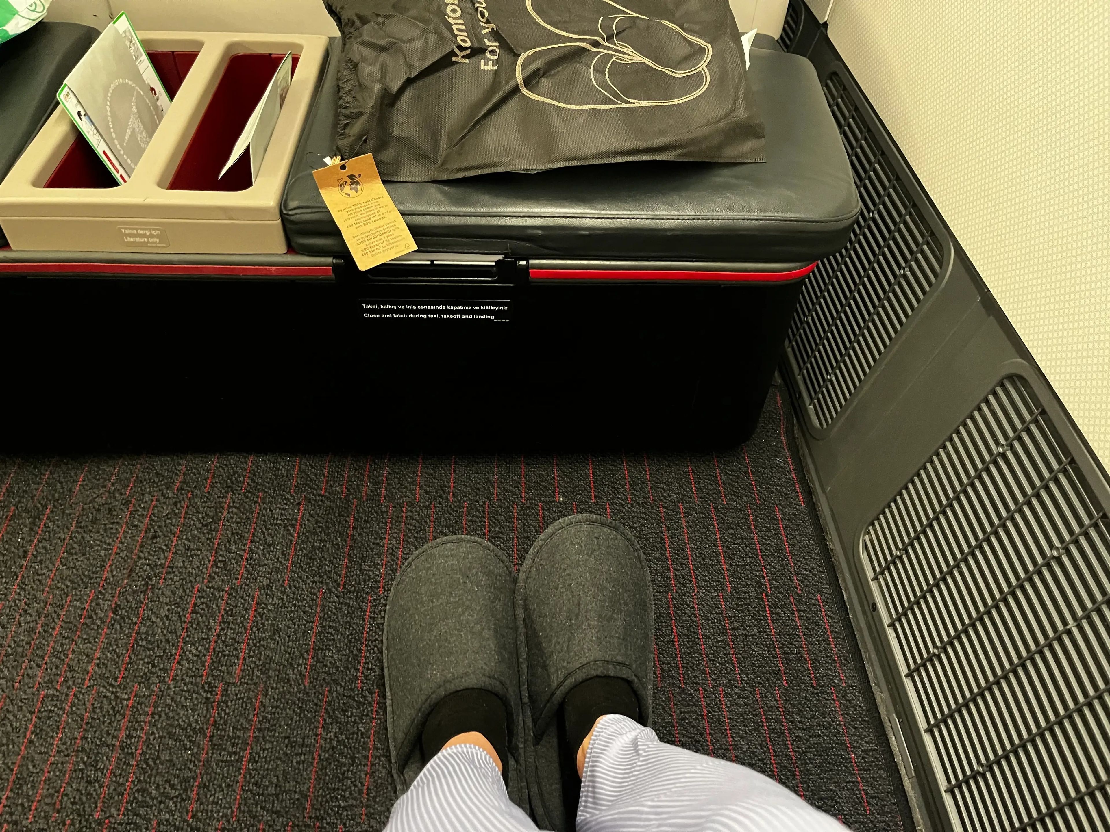 The writer's feet in black slippers and a black box with amenities in front of her on flight