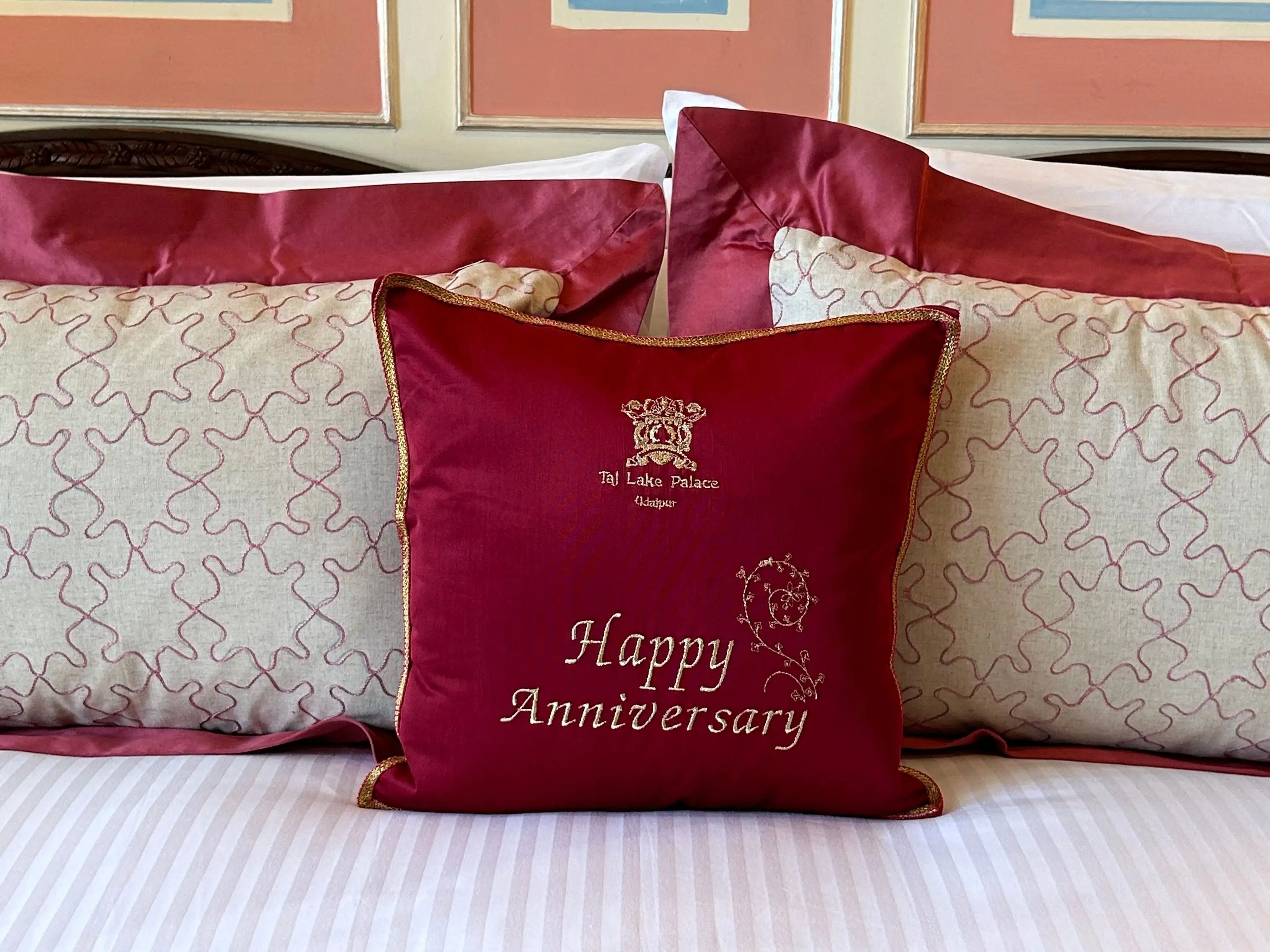 A bed with gold and red pillows. The pillow at the front reads "Happy Anniversary."