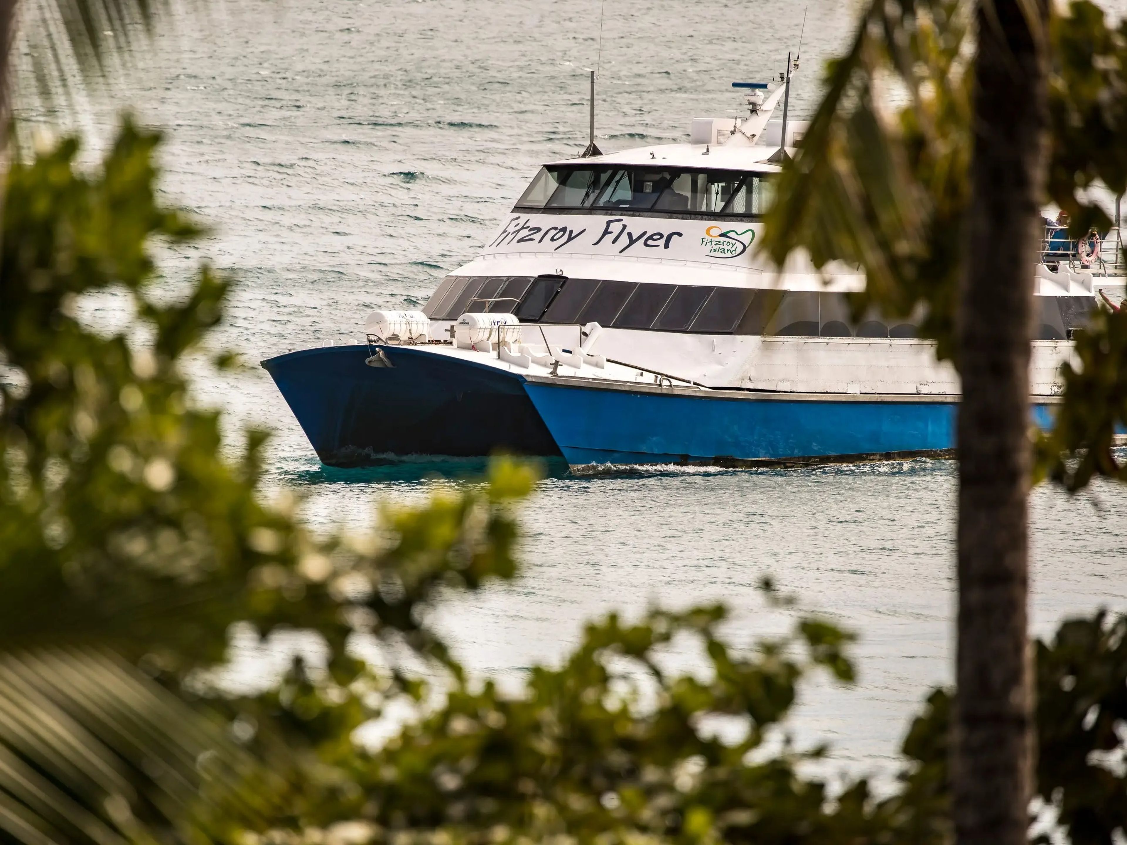 A boat called the Fitzroy Flyer is seen in the water through the trees.