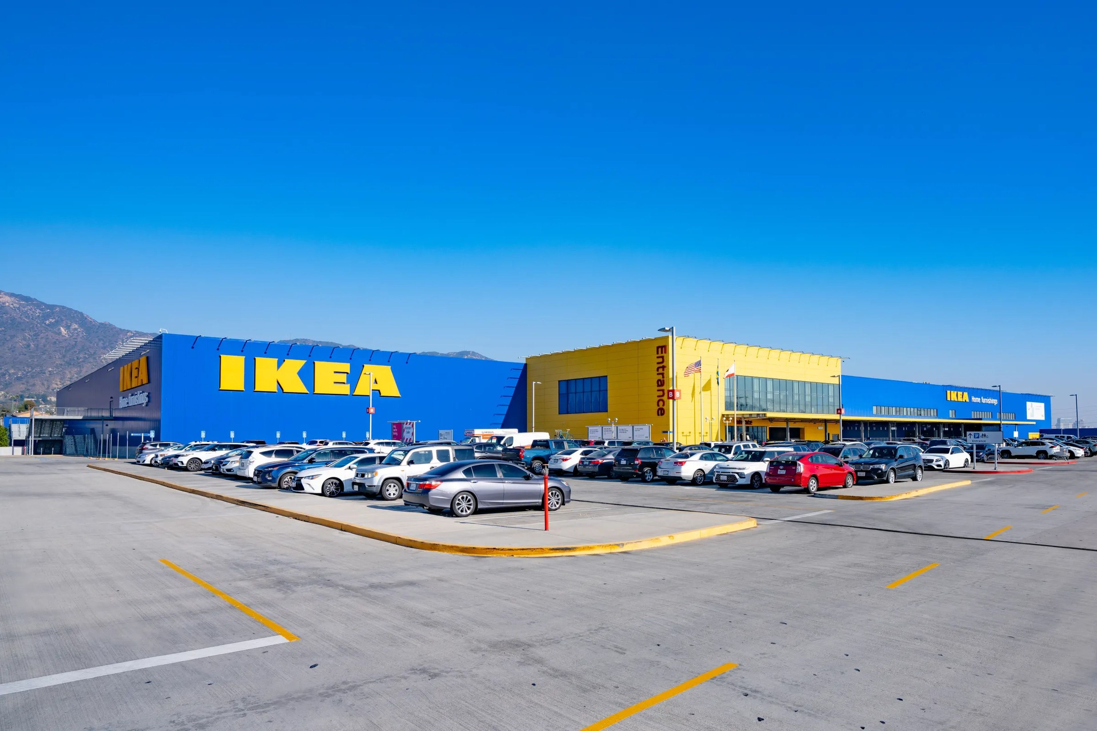 Cars sit parked outside of an Ikea store in California. The store is painted in the retailer's blue and yellow colors, and a sign that says "Entrance" is visible near the center of the building.