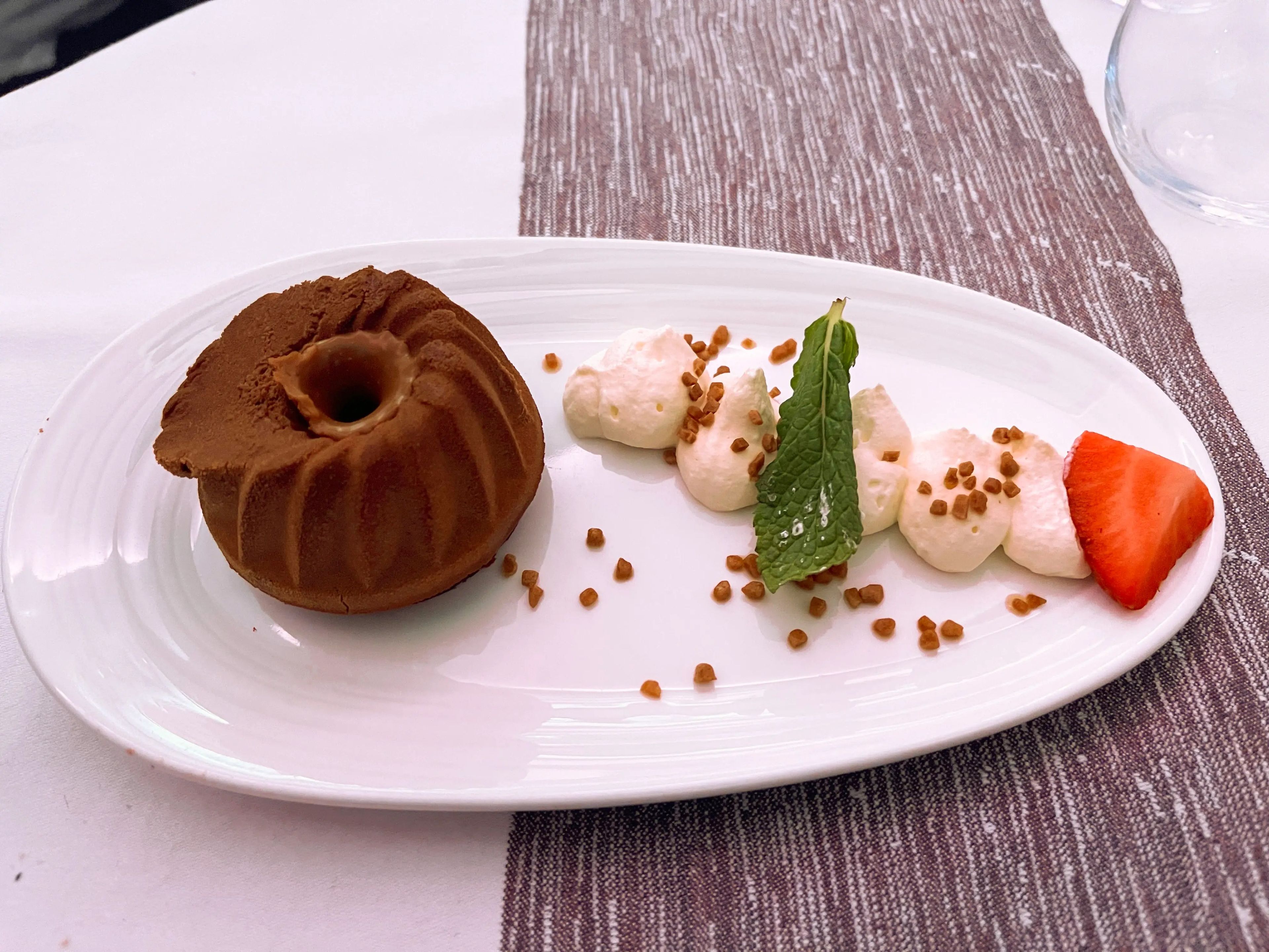 Chocolate-and-salted-caramel mousse with a wedge of strawberry and a mint leaf. The chocolate mouse is in the shape of a bundt and mouse is dotted along the opposite side of the plate