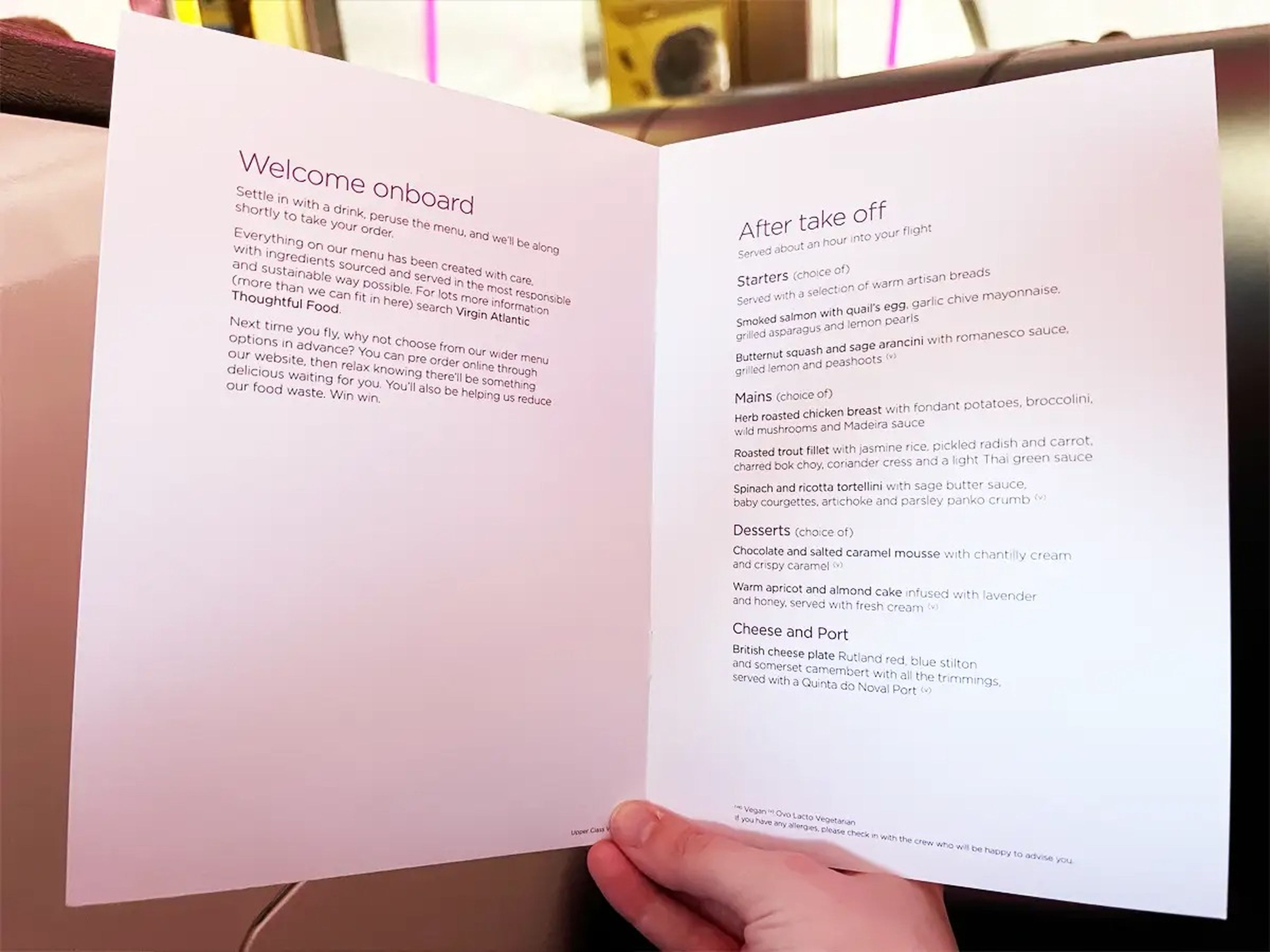 A hand holds a white paper menu with a "welcome onboard message" and a menu under a "after take off" section. The menu includes starters, mains, desserts, and cheese and port