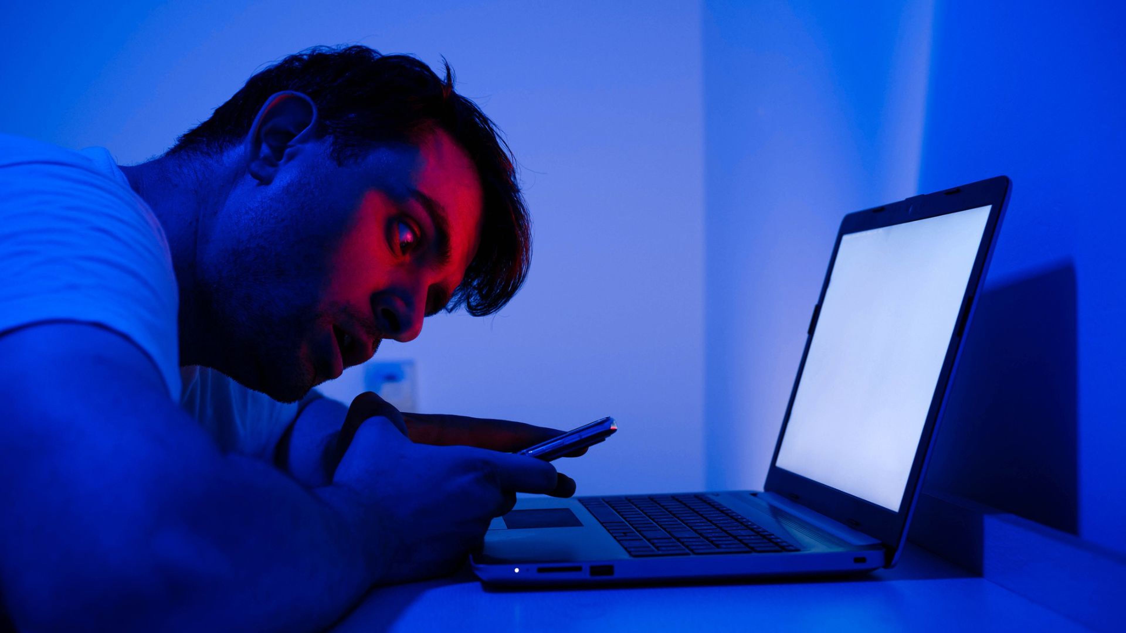 Un hombre con cara de susto delante de un ordenador y con un teléfono móvil.