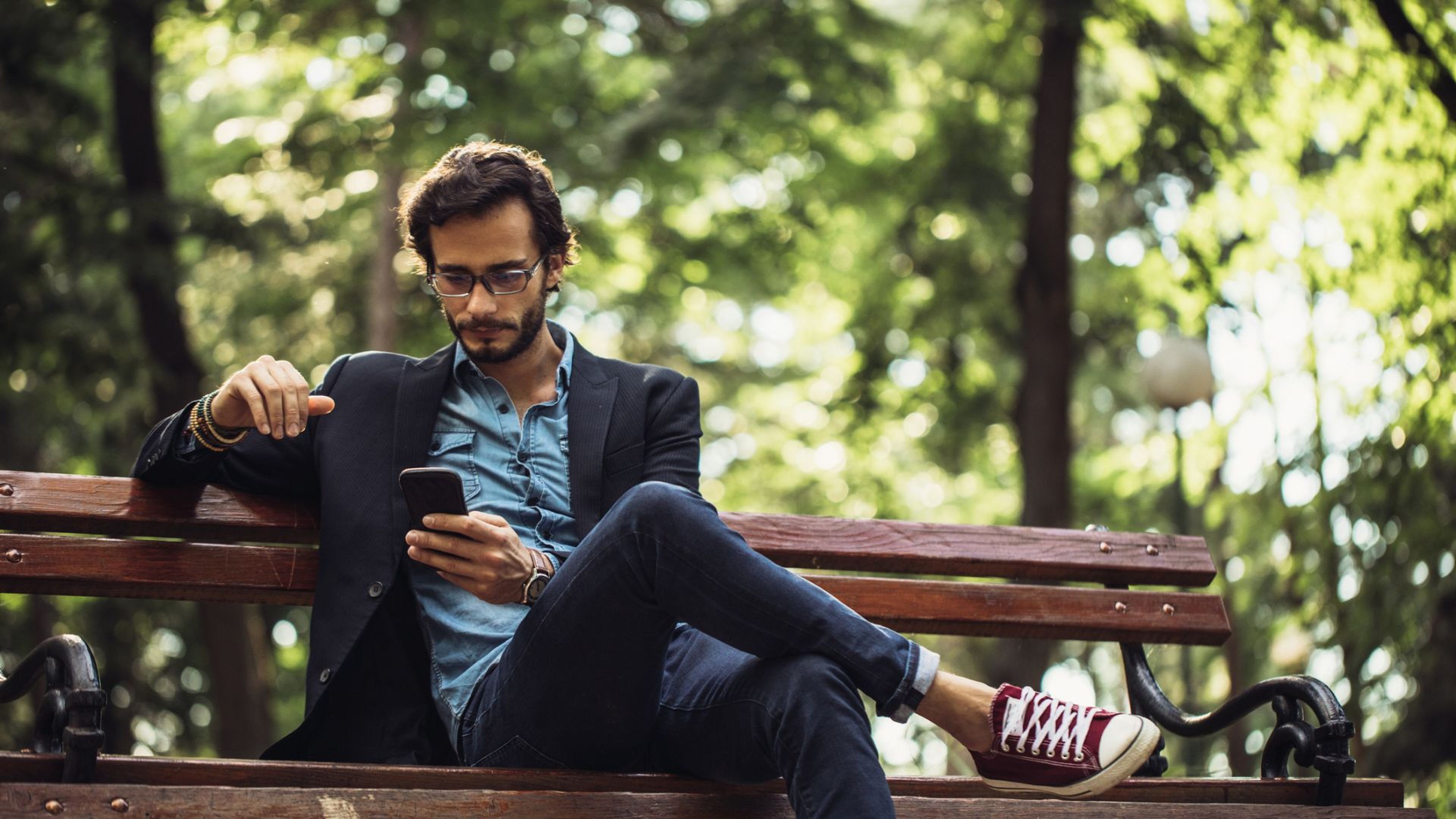 Un hombre consulta el móvil sentado en un banco del parque.
