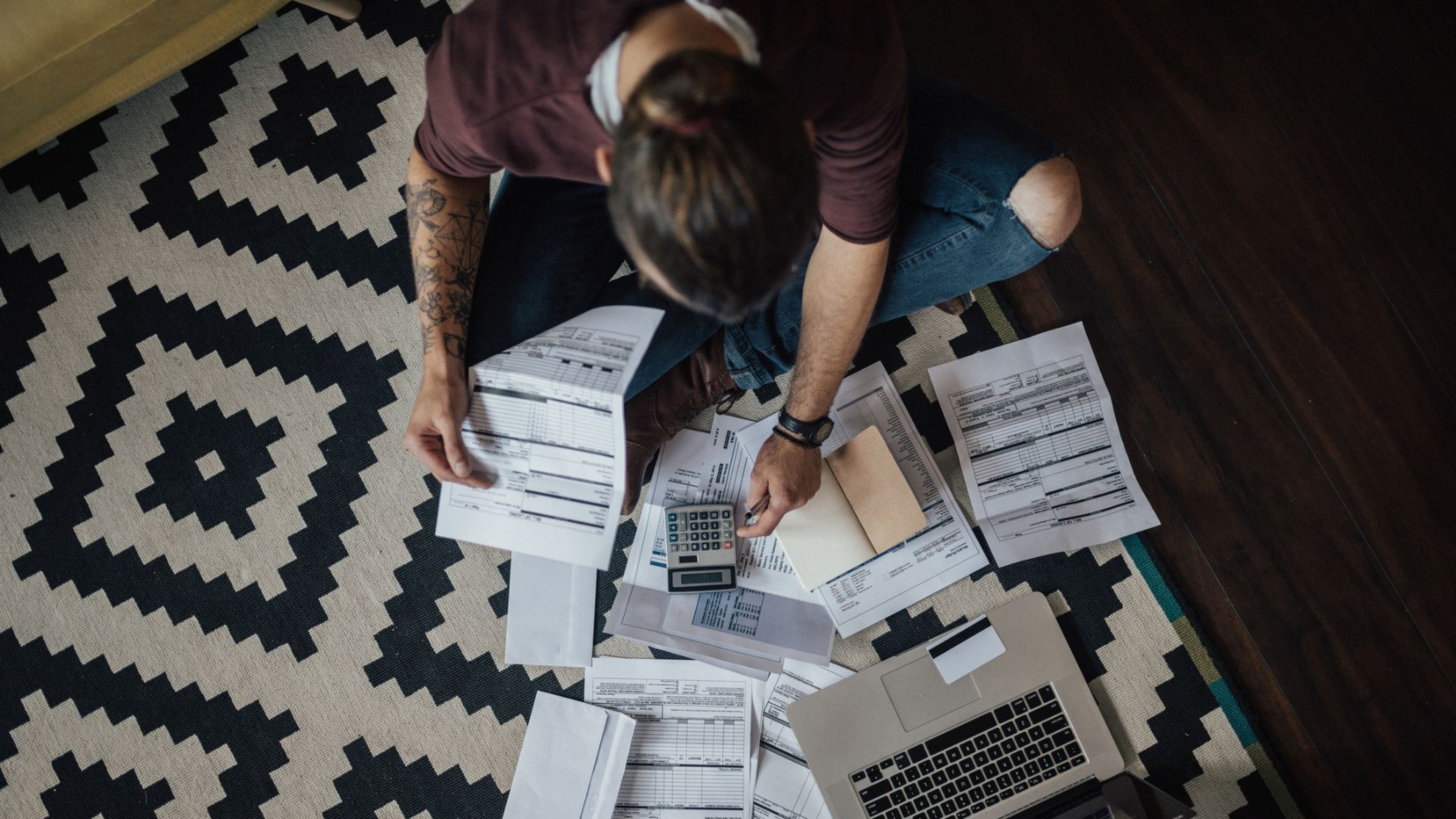 Un hombre trabaja sobre un alfombra con papeles, ordenador y una calculadora.
