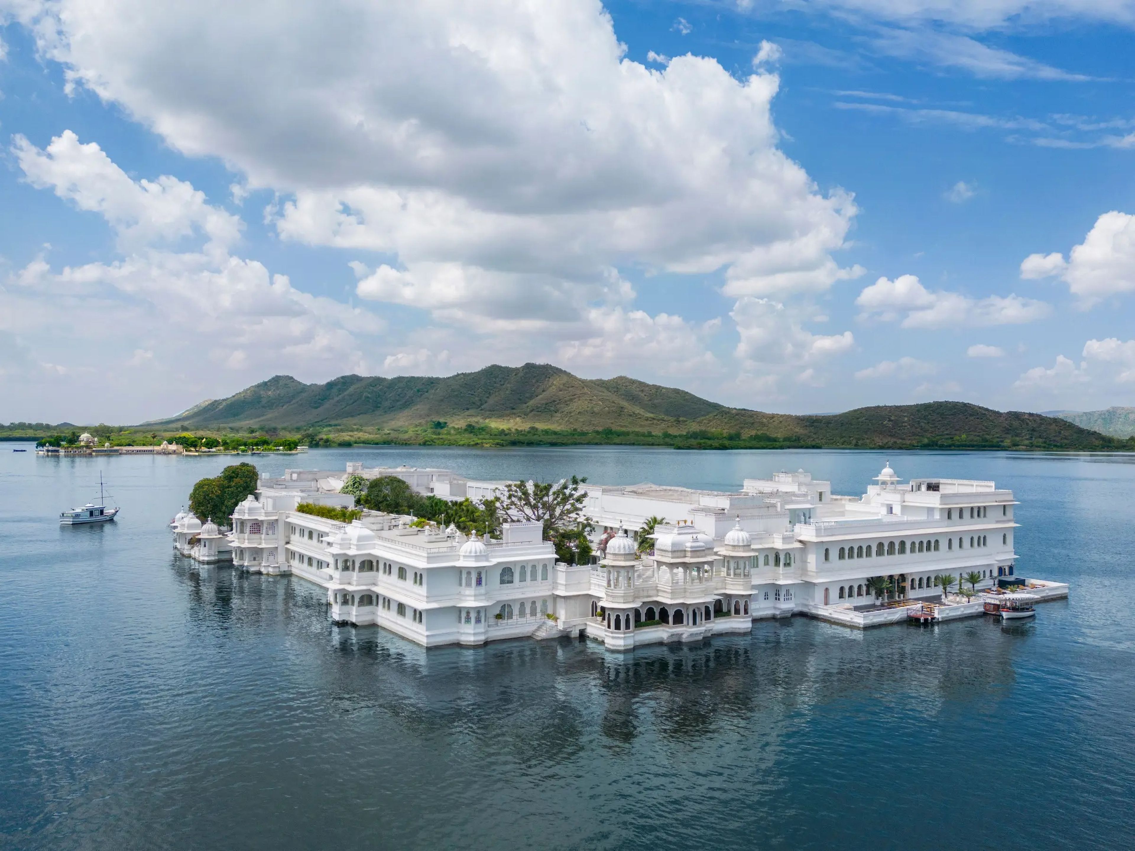 A large white hotel located in the middle of a lake with mountains in the background.