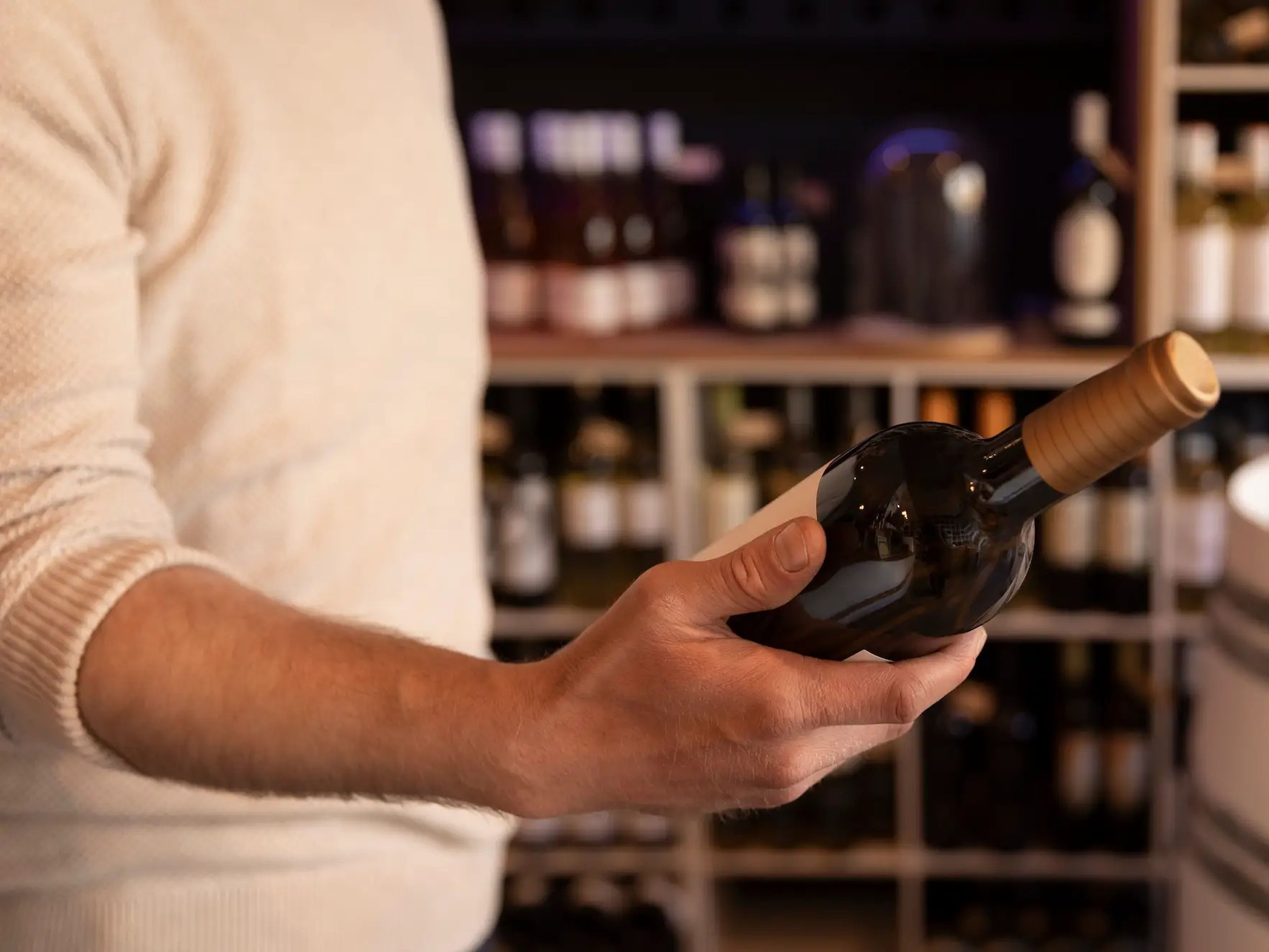 A man holding a wine bottle in a liquor wine shop with shelves of bottles in the background.