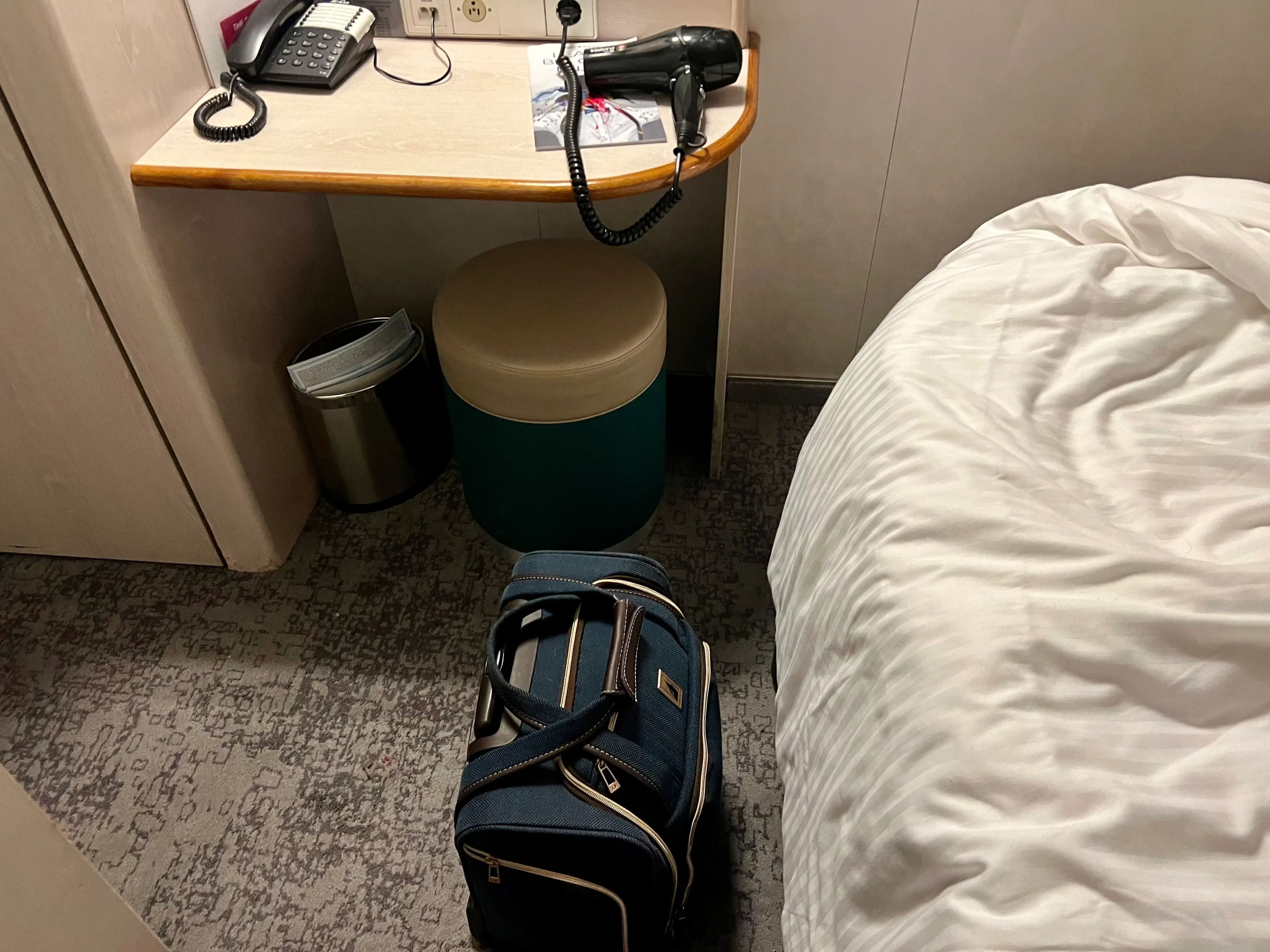 My suitcase on the carpet next to the foot of the bed.
