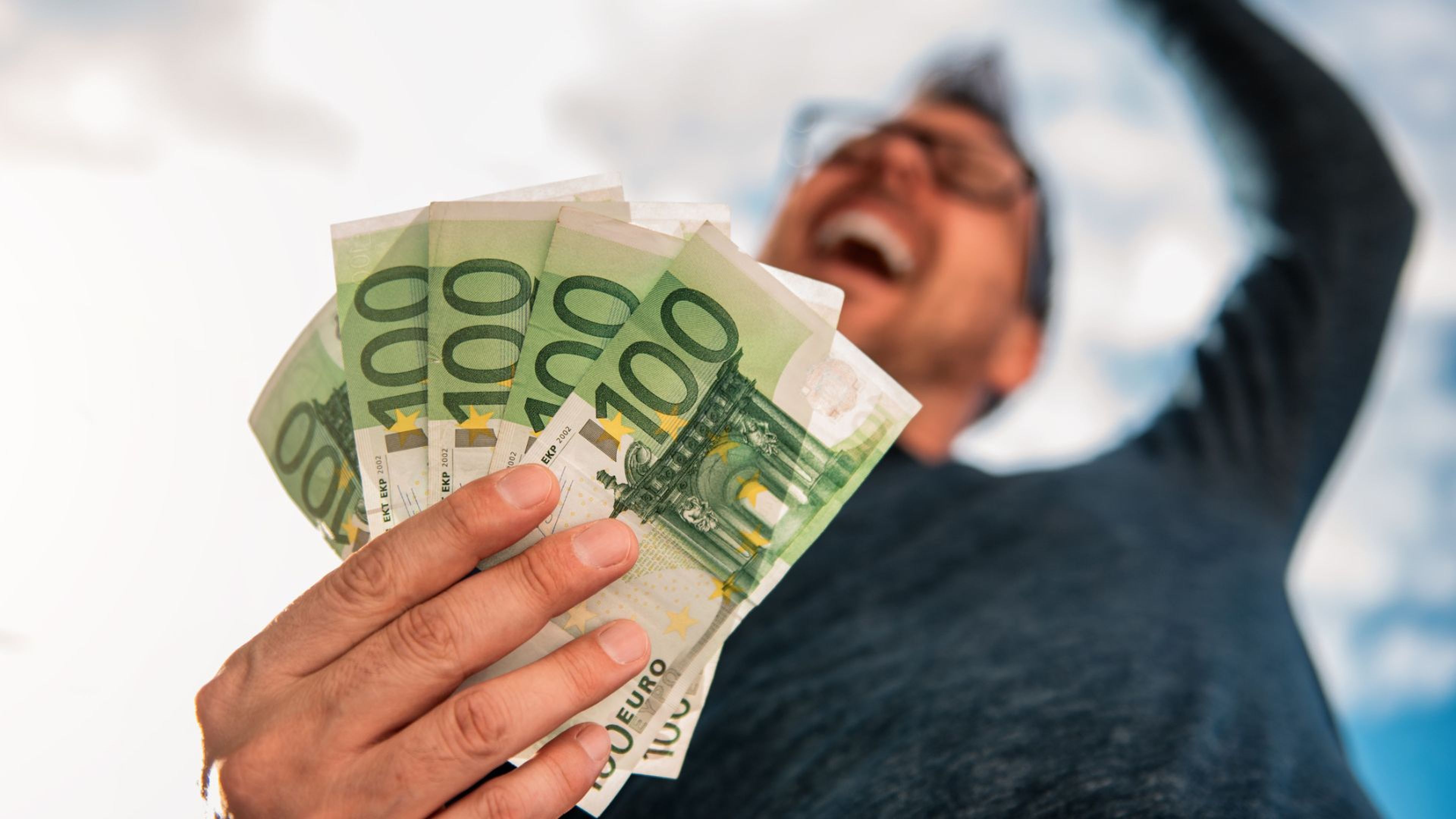 Una persona muy contenta con varios billetes de 100 euros en la mano.