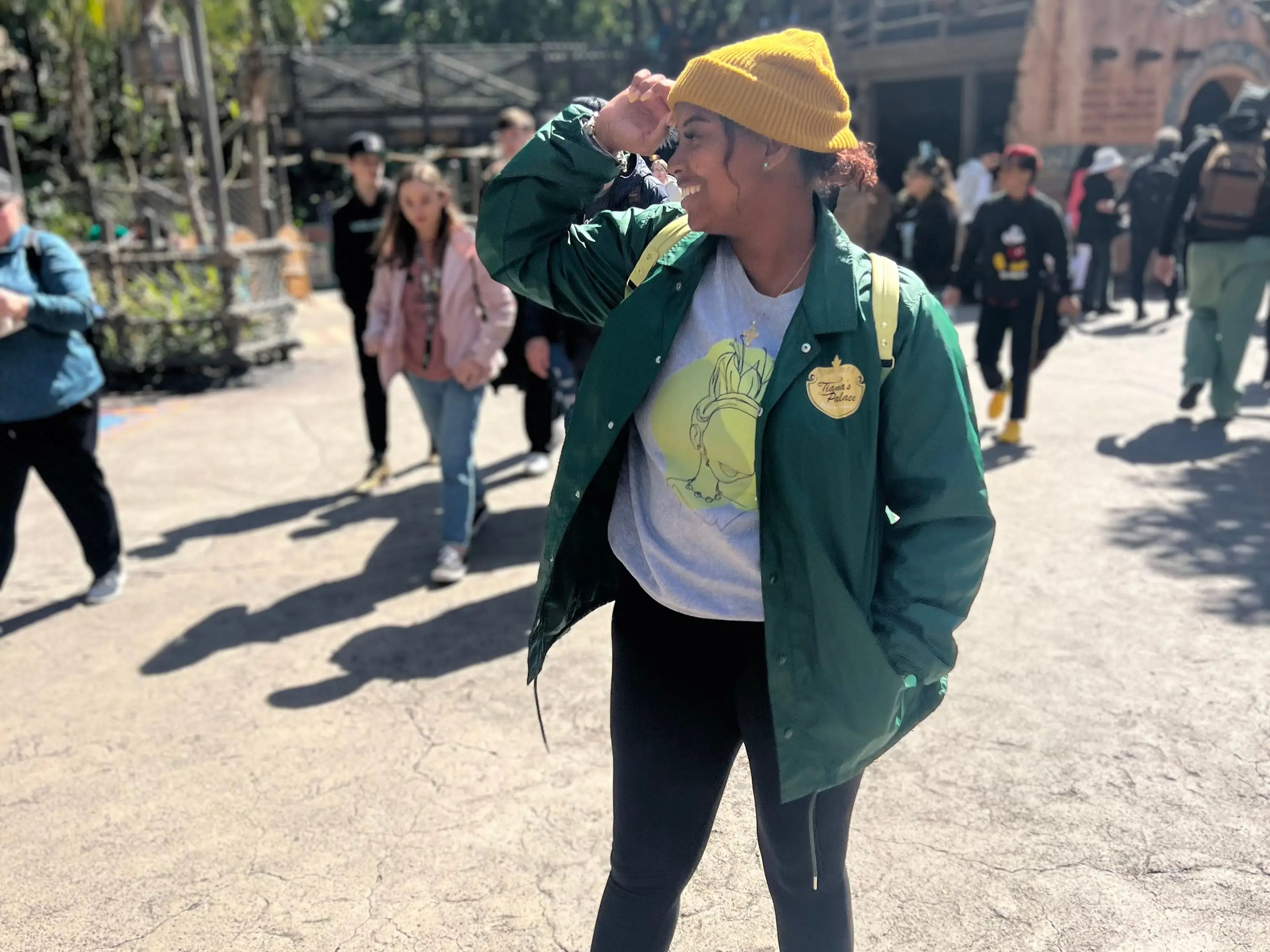 Photo of the writer smiling and holding her hand to her eyes at Disneyland. The writer wears black leggings, a gray short, a green jacket, and a yellow beanie