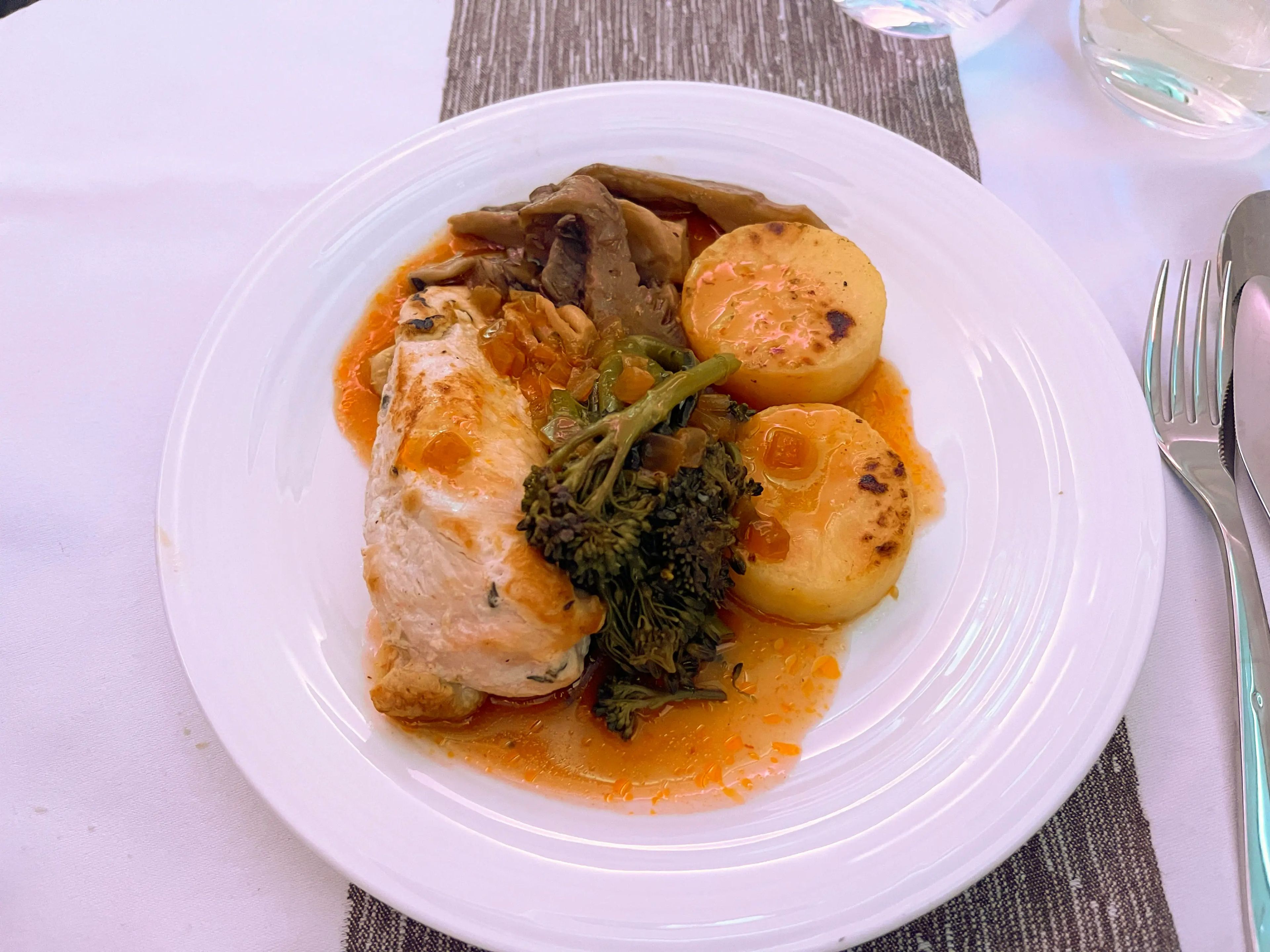 Roasted chicken breast with fondant potatoes, Broccolini, mushrooms, and Madeira sauce on a white plate