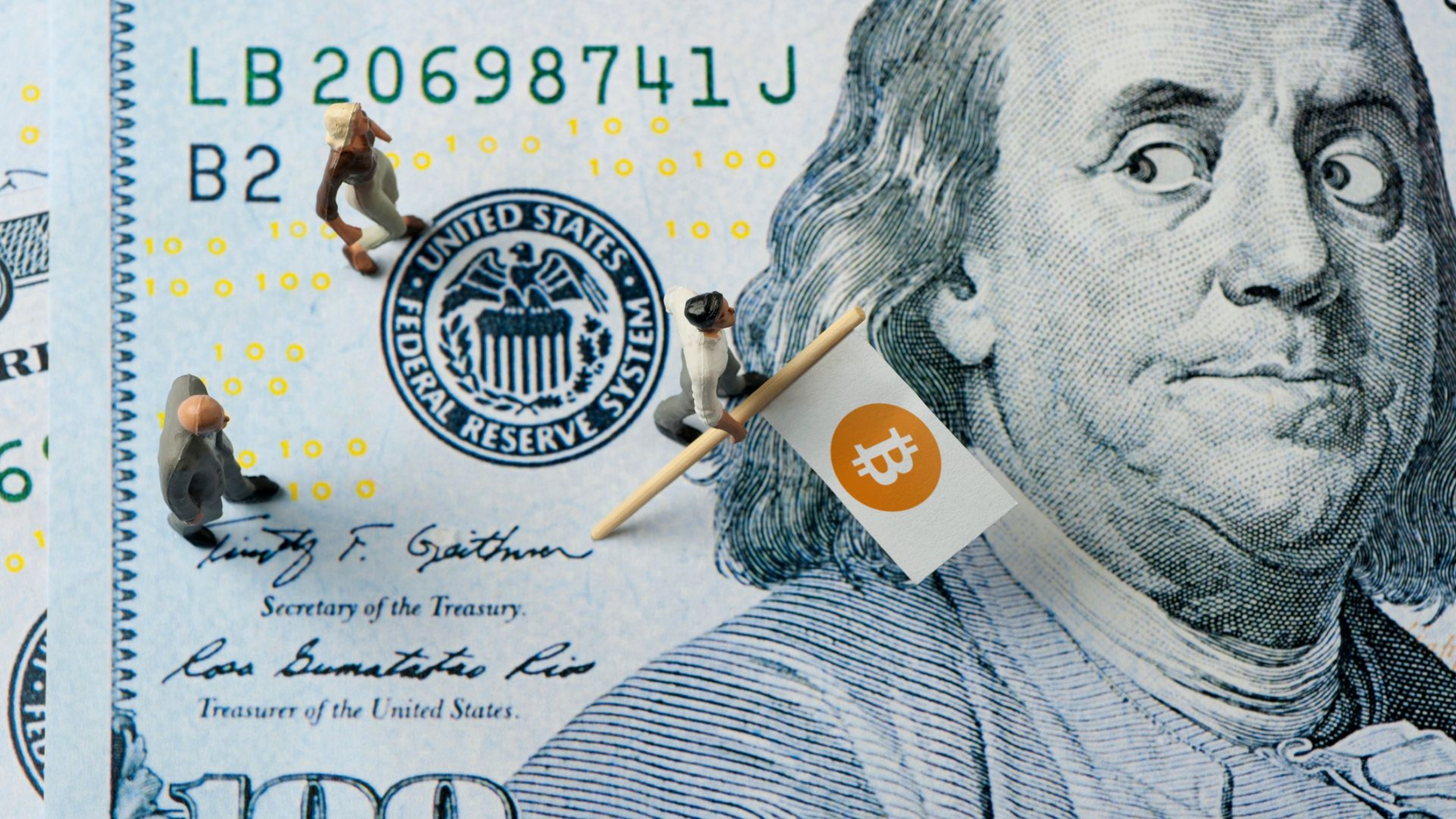 Varios muñecos con la bandera de bitcoin encima de un billete de dólar.
