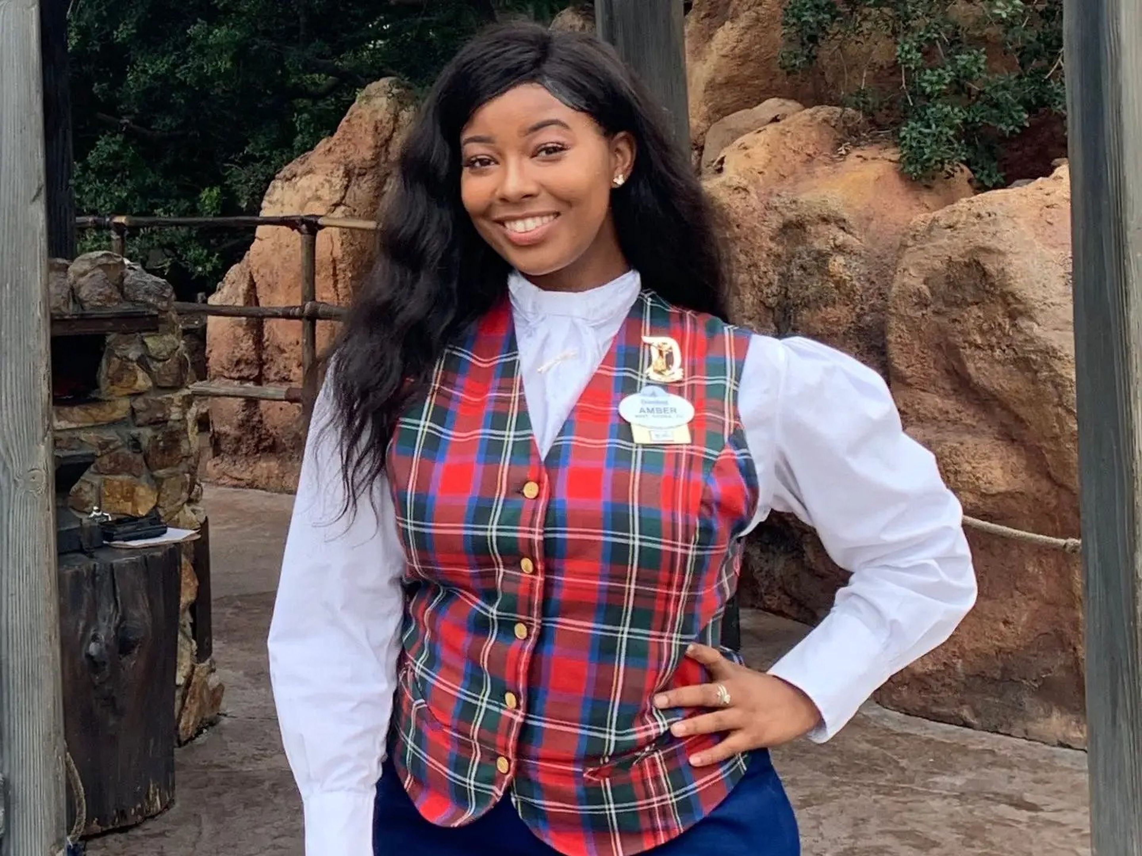 The writer wears a VIP Disneyland tour guide uniform, which includes a red plaid vest, a white shirt, and a blue skirt, and smiles