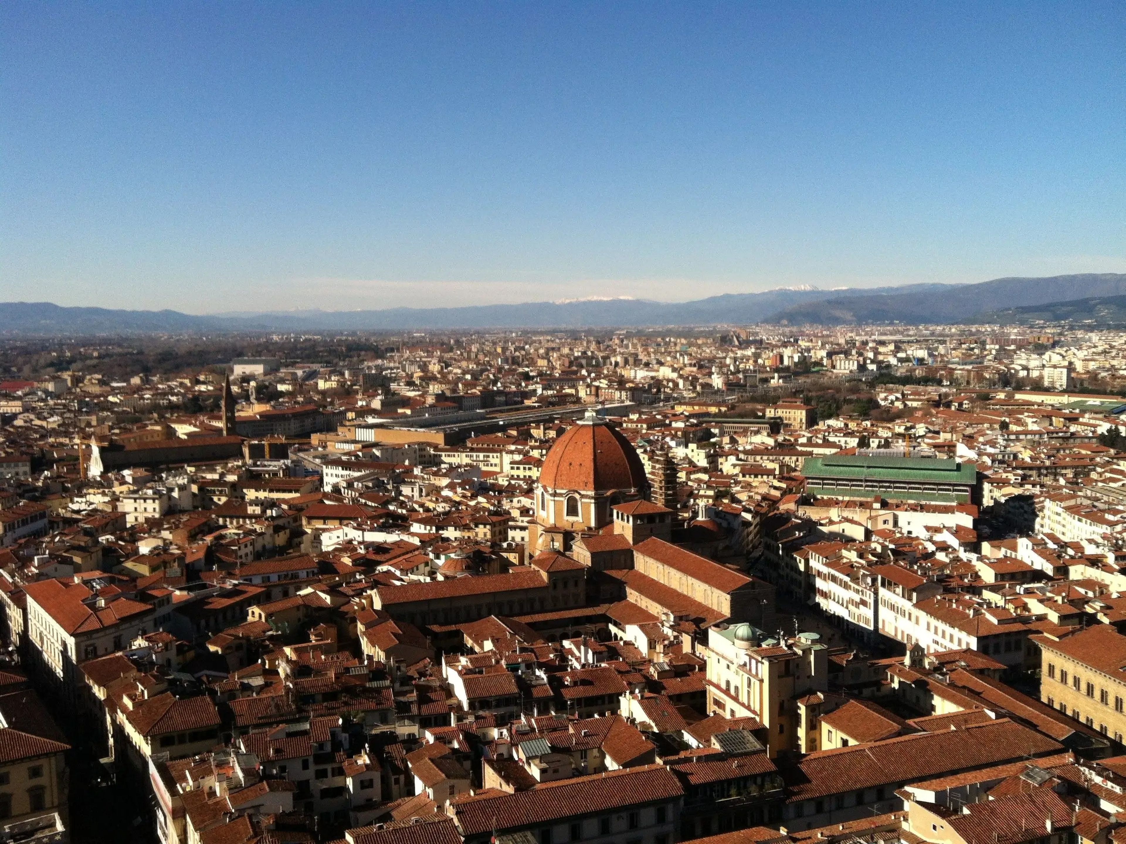 An aerial view of buildings in Florence, Italy, with mountains in the background.
