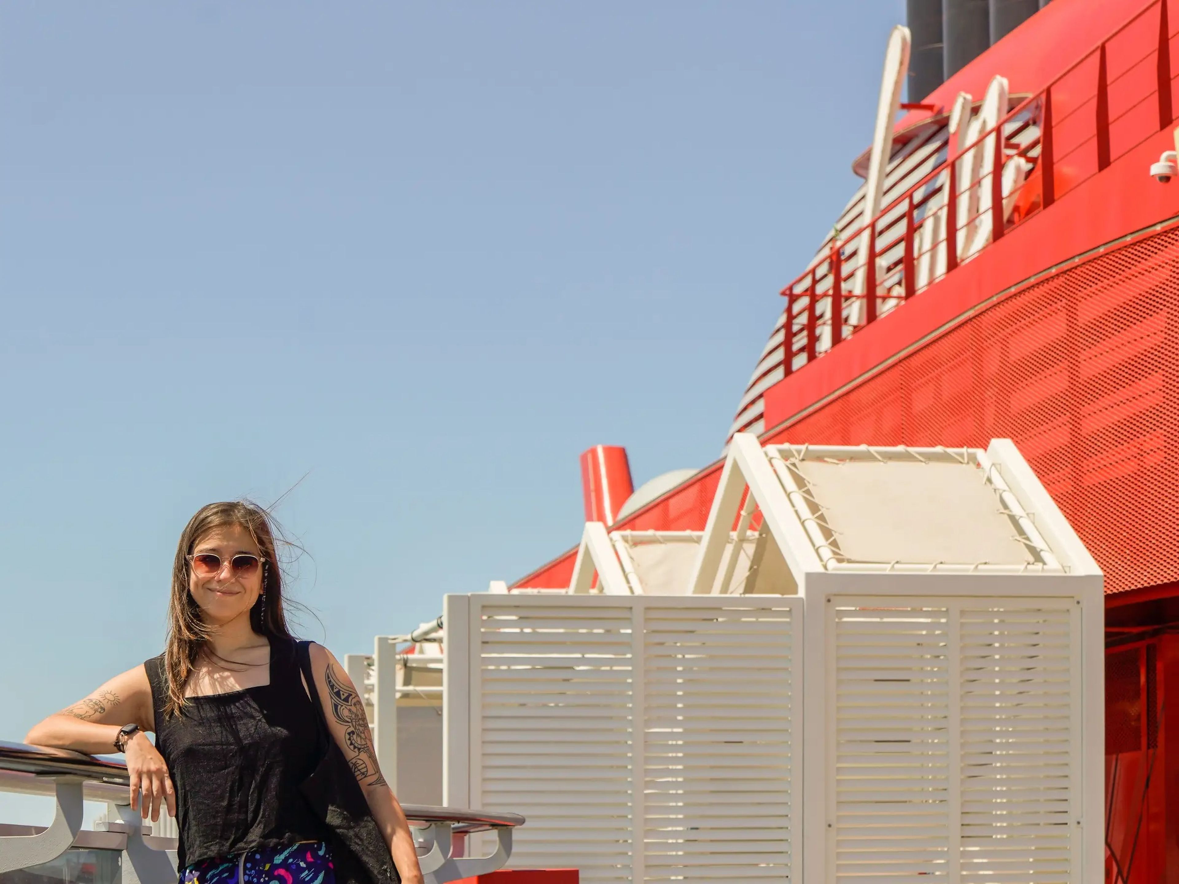 The author leans against the side of a cruise ship with blue skies behind her.