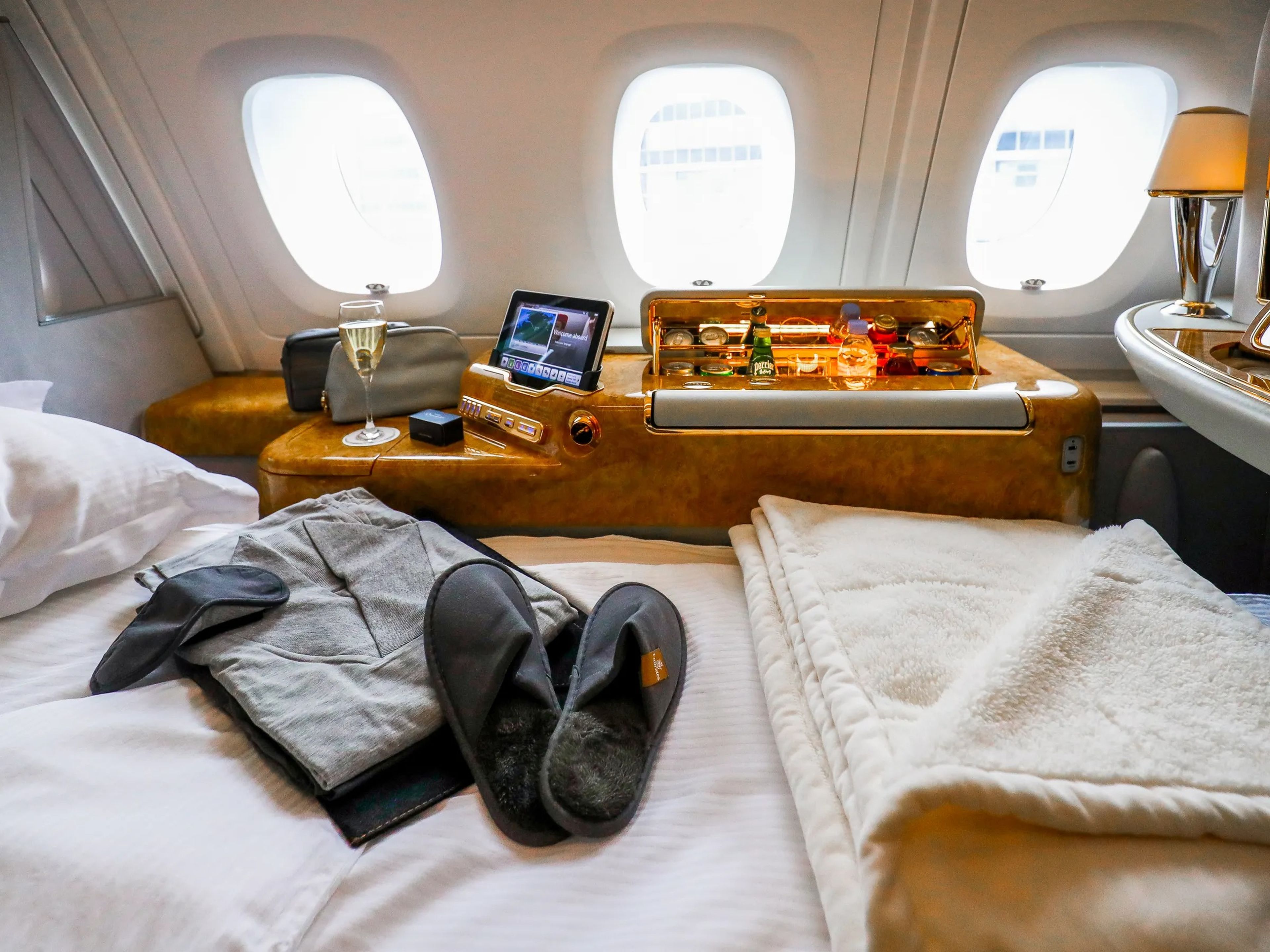 A bed, slippers, a blanket, a robe, and a sleep mask on a bed inside the first class cabin inside an Airbus A380 at the airbus factories in Hamburg, Germany, Reefrreshments in the background in front of three windows