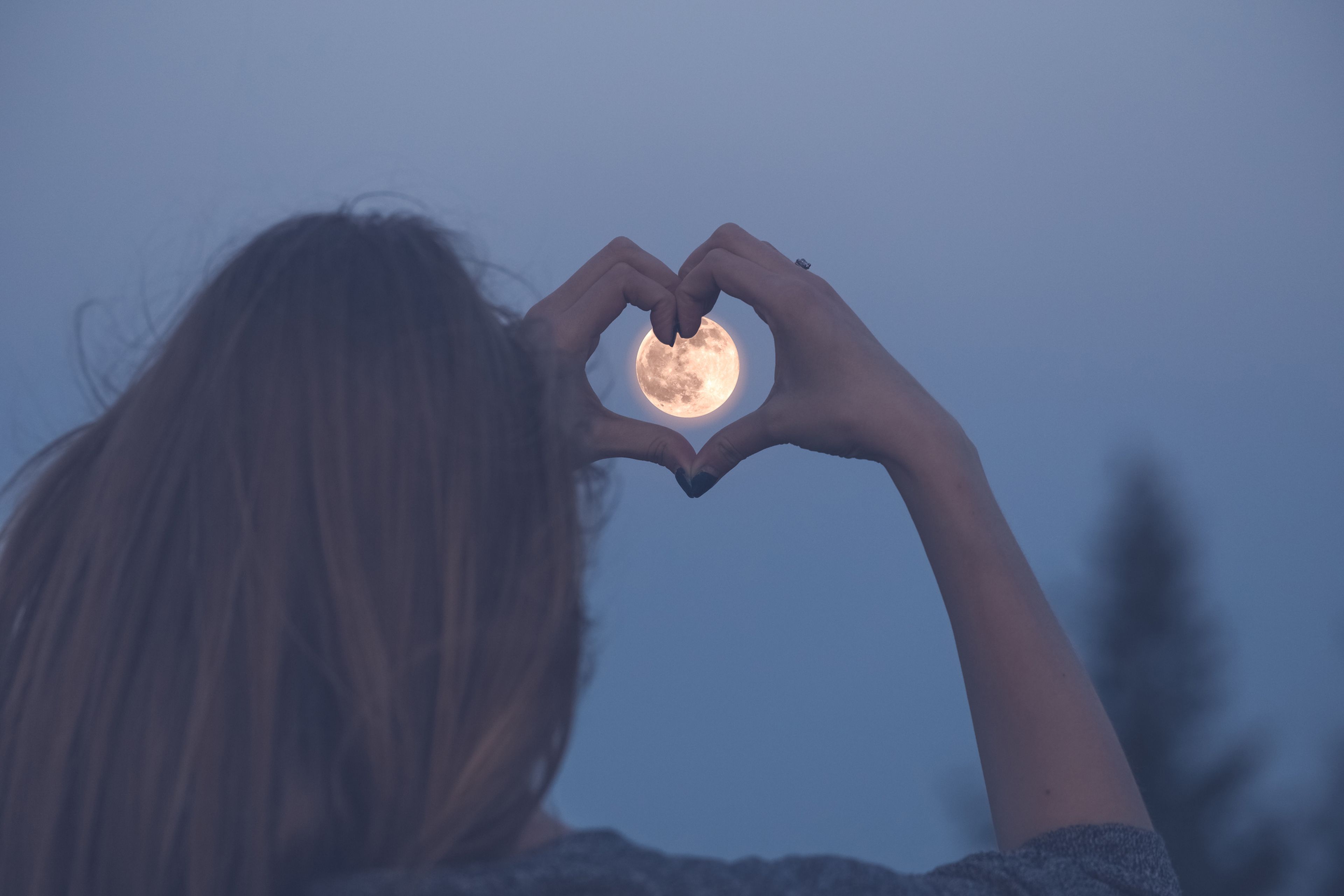 Chica haciendo un corazón con la Luna de fondo