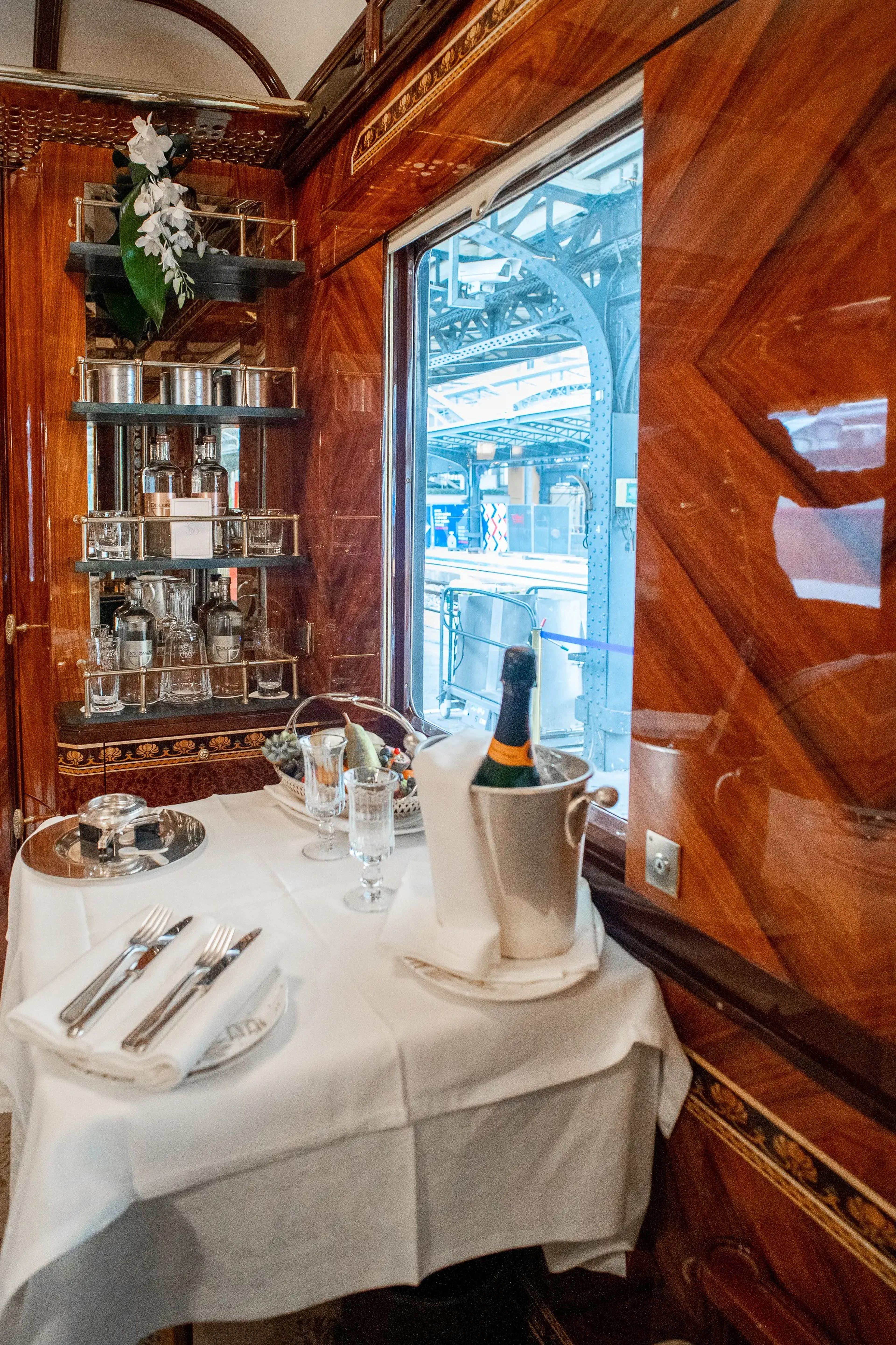 dining table with a white cloth and champagne in front of a bar against the wall in a wood-walled train cabin