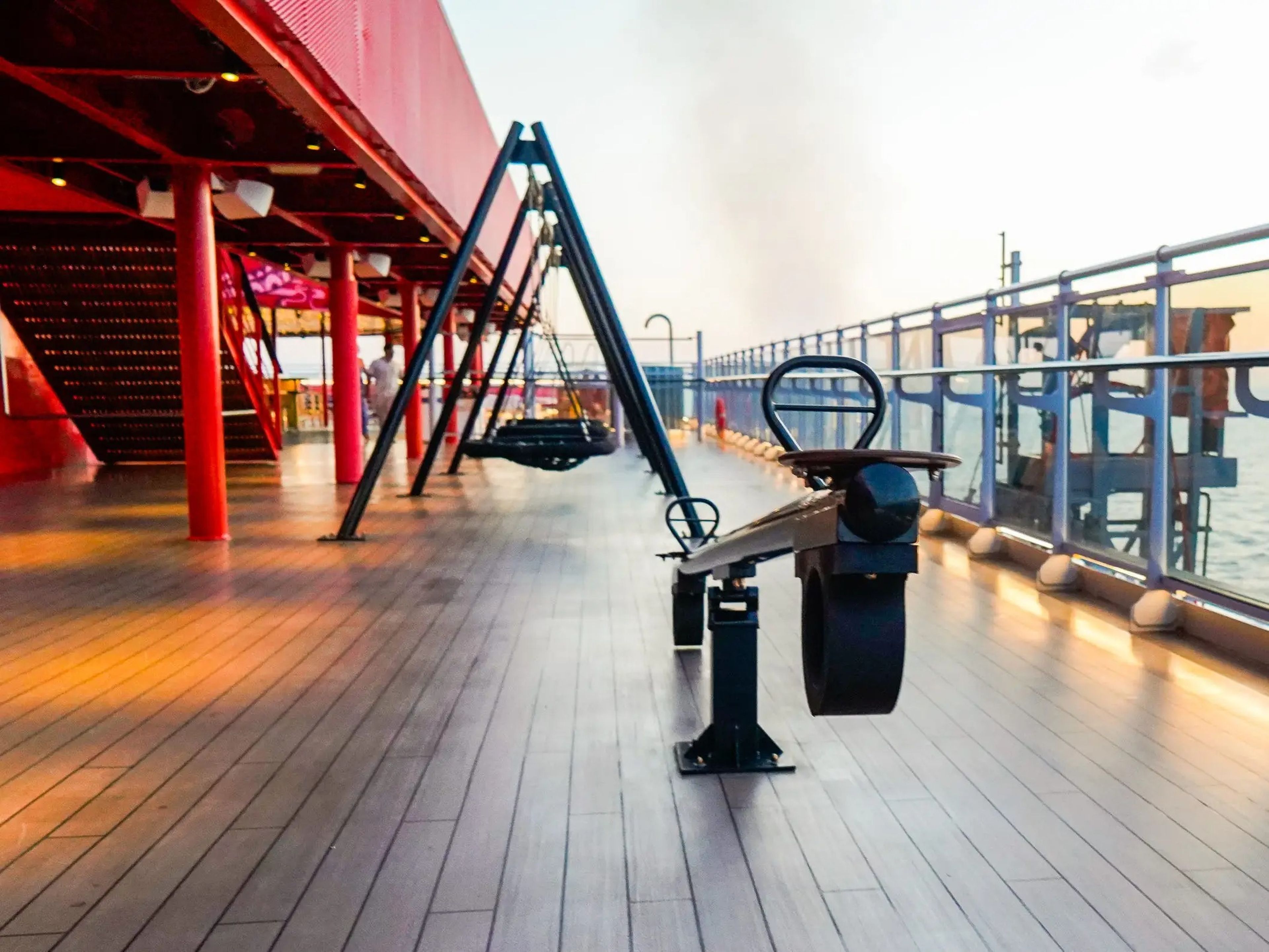 An empty deck on a cruise ship with a black seesaw, swings, and  a red staircase