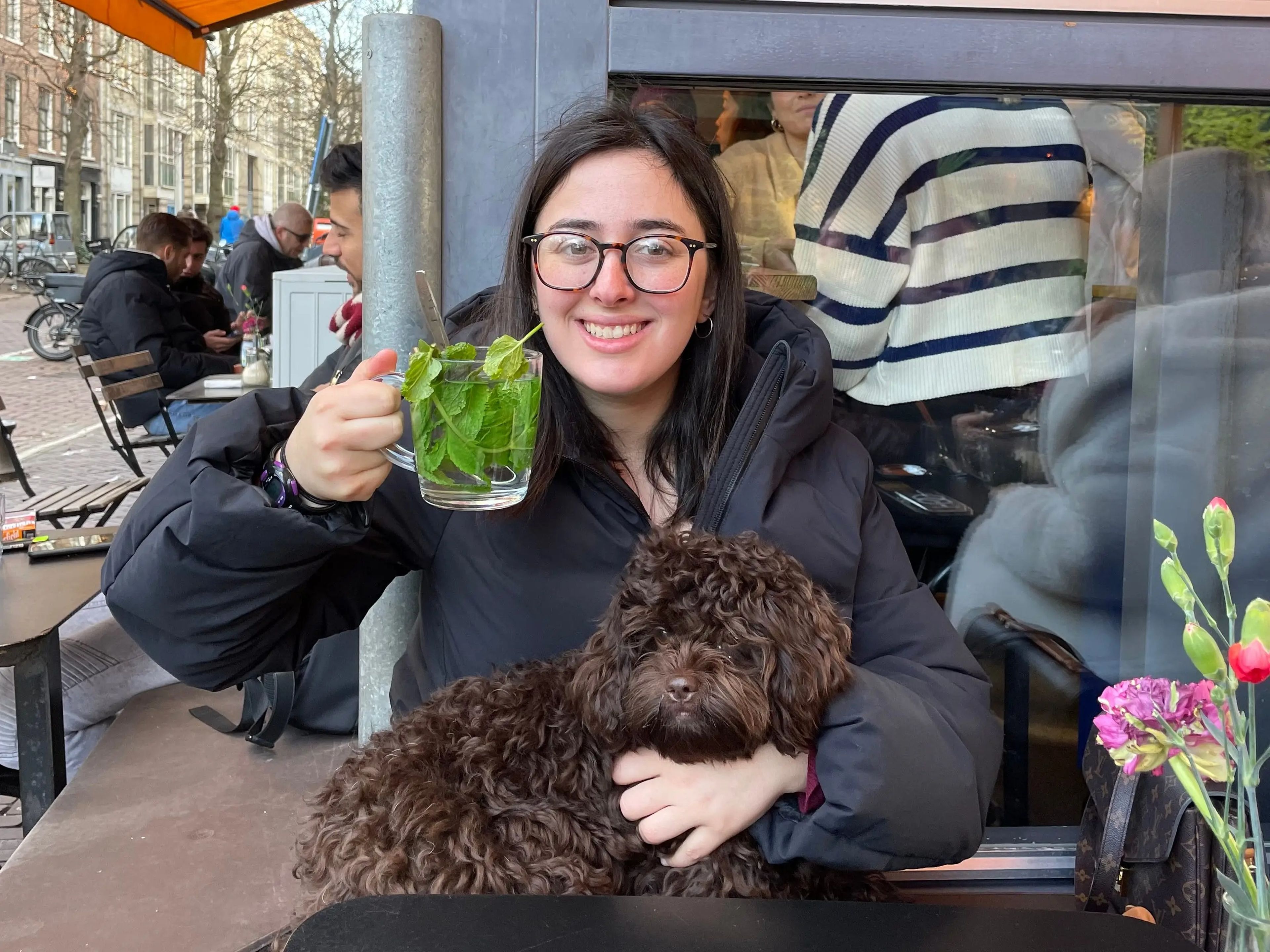hannah holding a class of green tea with a dog on her lap at a restaurant in europe