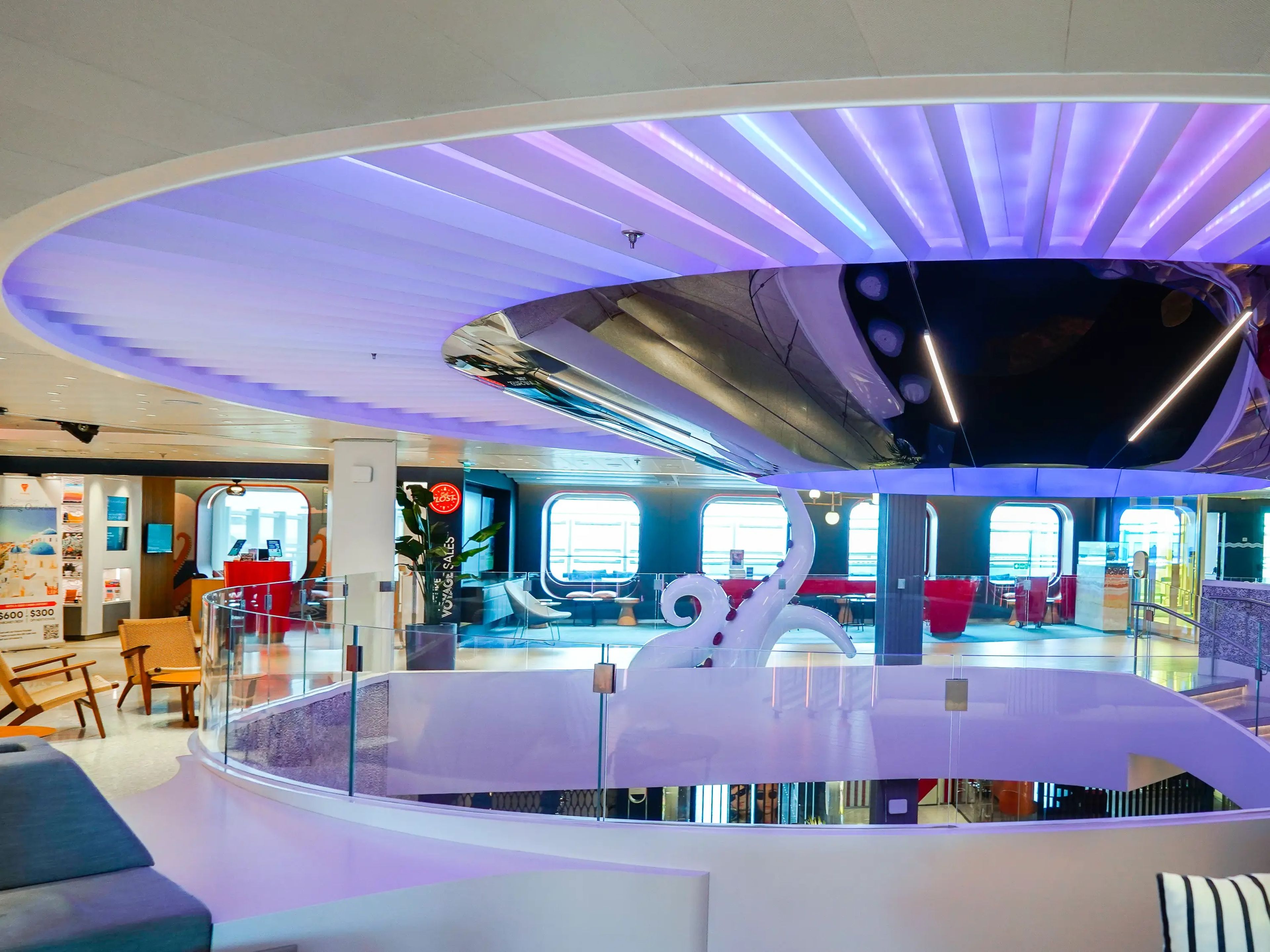 Inside. a cruise ship lobby are white walls and a circular ceiling feature with blue and purple lights shining down