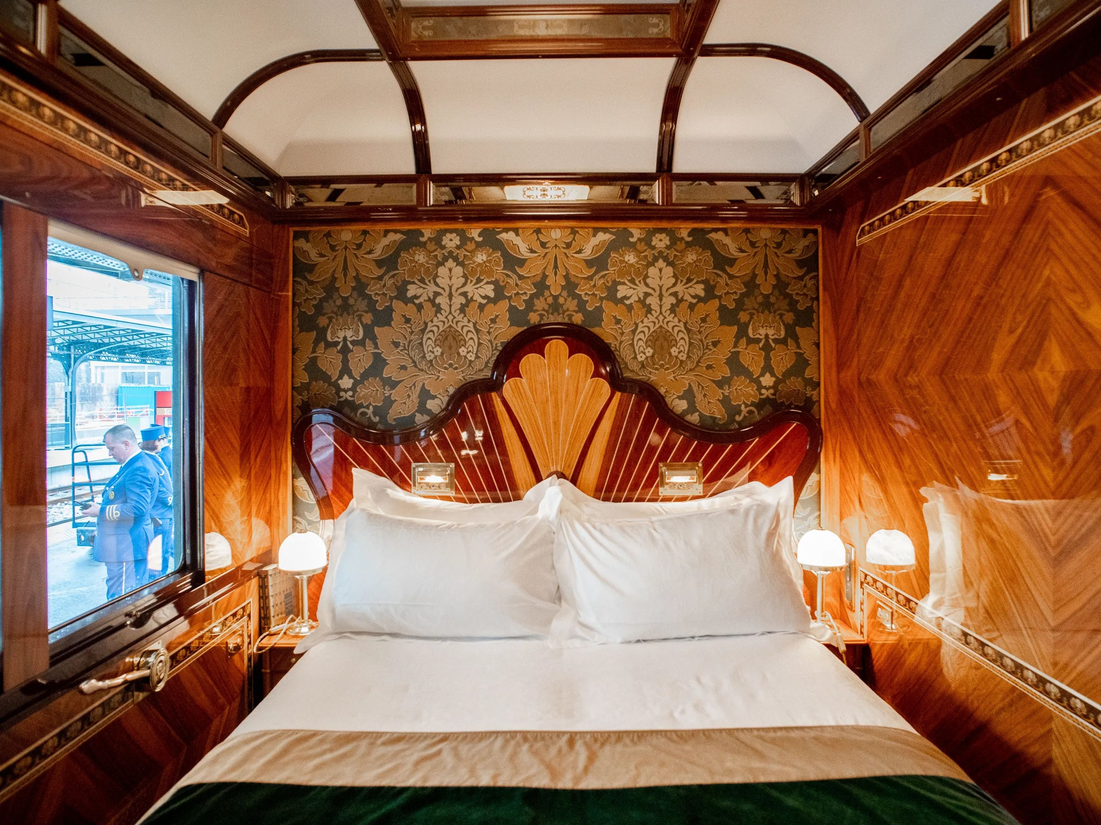 Inside a wood-walled train suite with white and green furnishings and a bed in the back center.