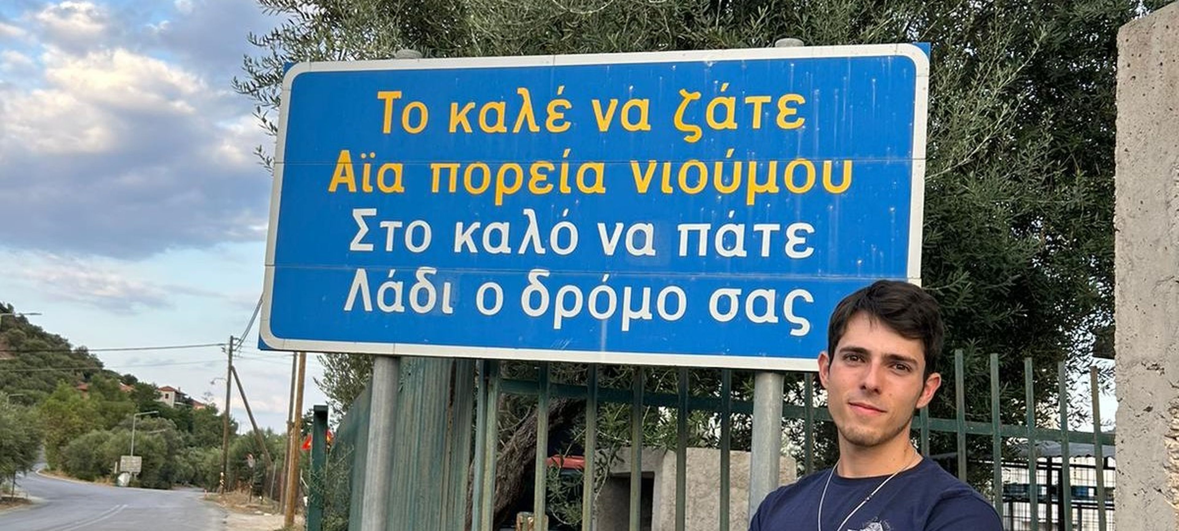 Jaime García Chaparro posa en la pueblo de Leonidio, Grecia, con un cartel que dice en griego moderno y en tsakonio: "Que te vaya bien. Que tu camino sea aceite". La expresión se utiiza para desear a alguien buen viaje.
