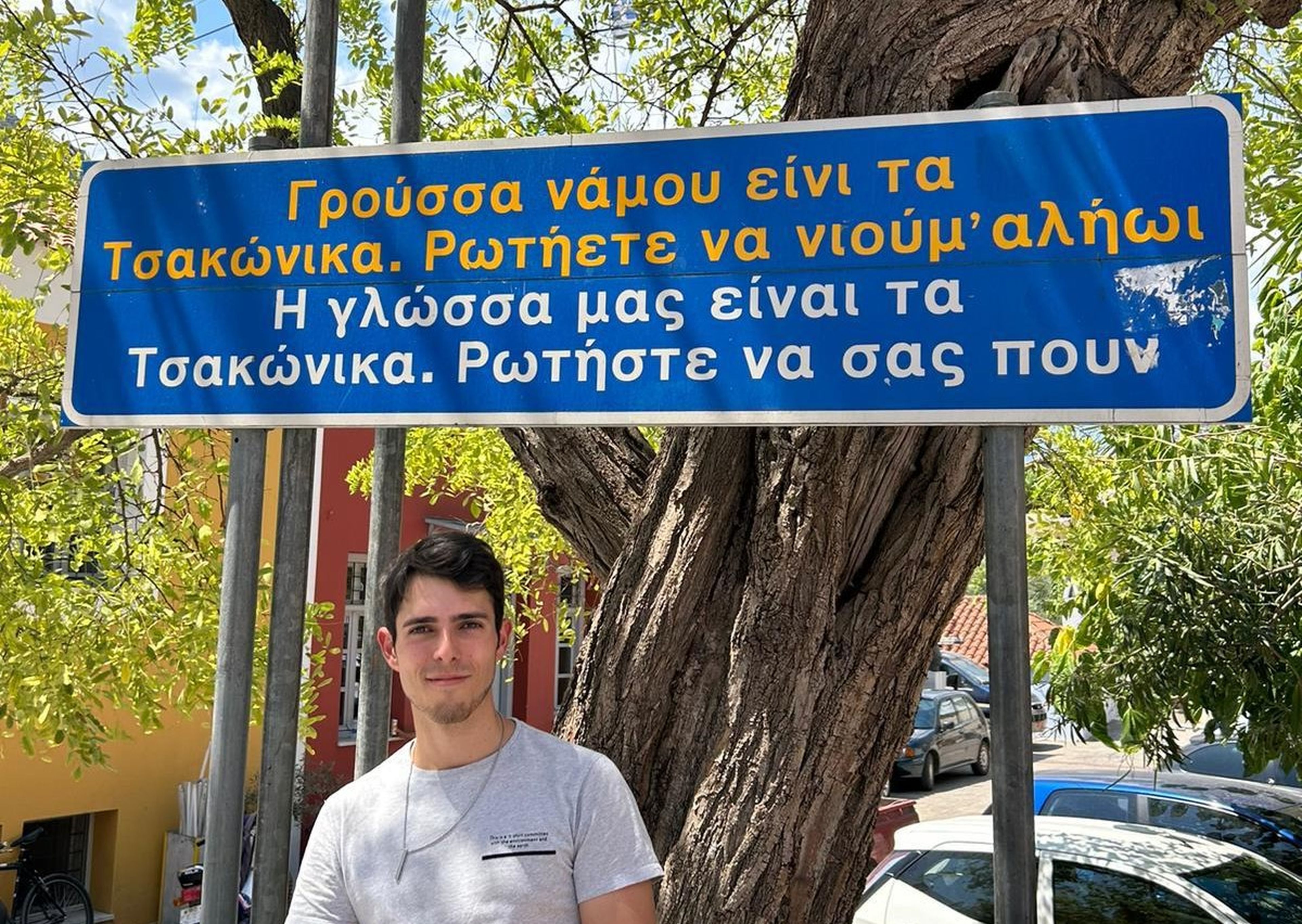 Jaime García Chaparro posa en el pueblo de Leonidio, en Grecia, ante un cartel que dice en griego moderno y en tsakonio: "Nuestra lengua es el tsakonio. Pregúntanos y te contaremos".