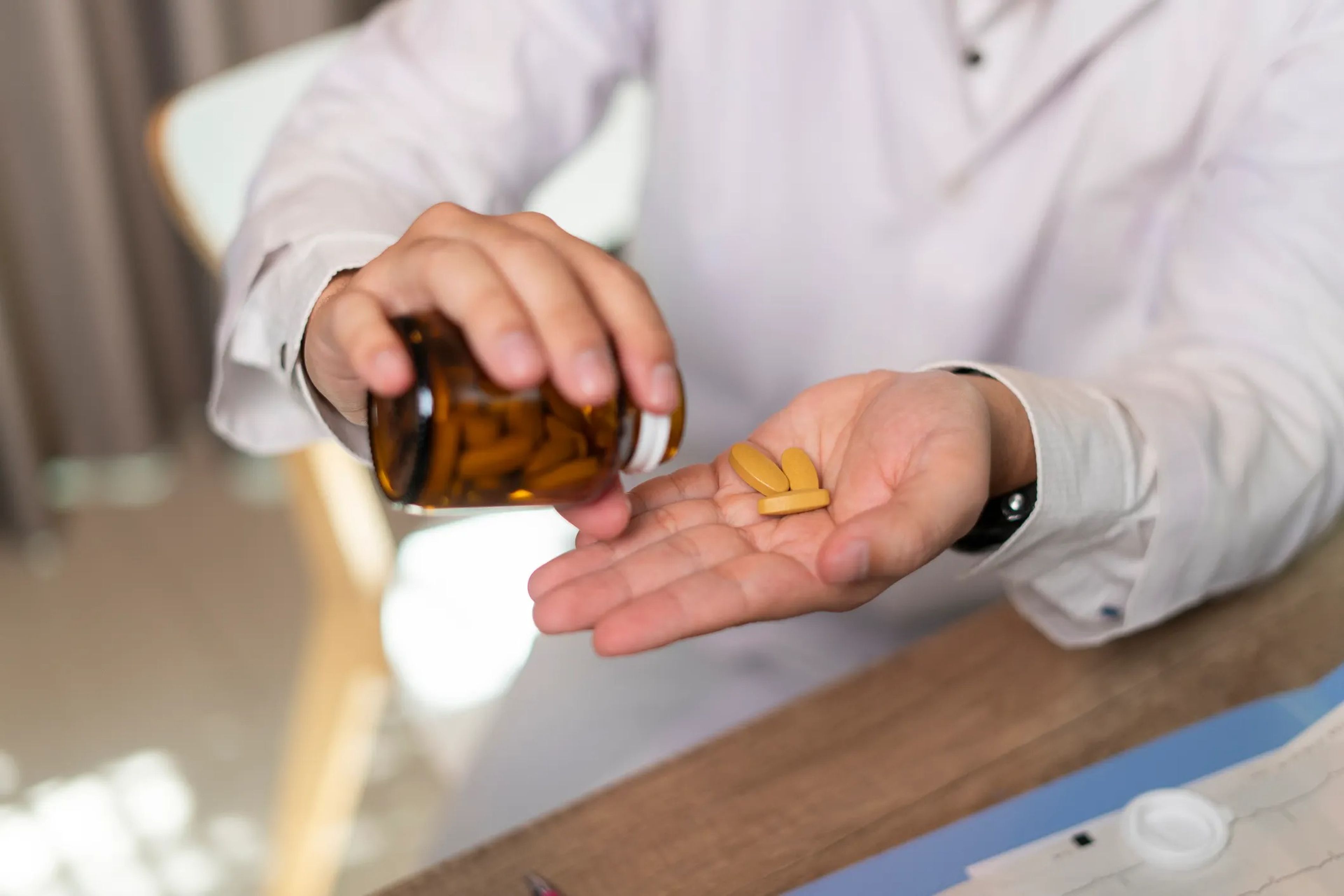 A man in a white lab coat pours yellow pills into his hand.