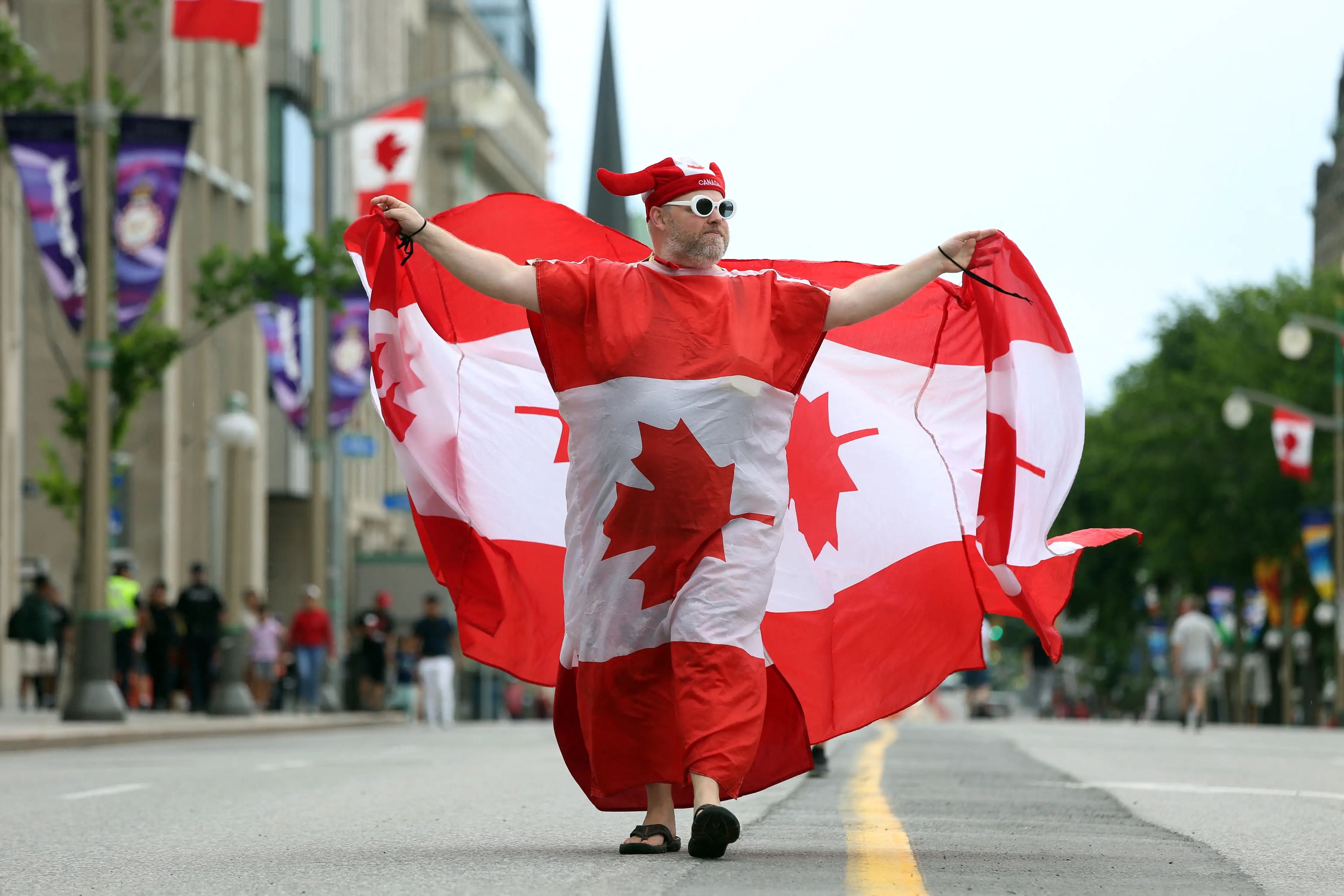 A man wrapped in two Canadian flag parades down an empty street.