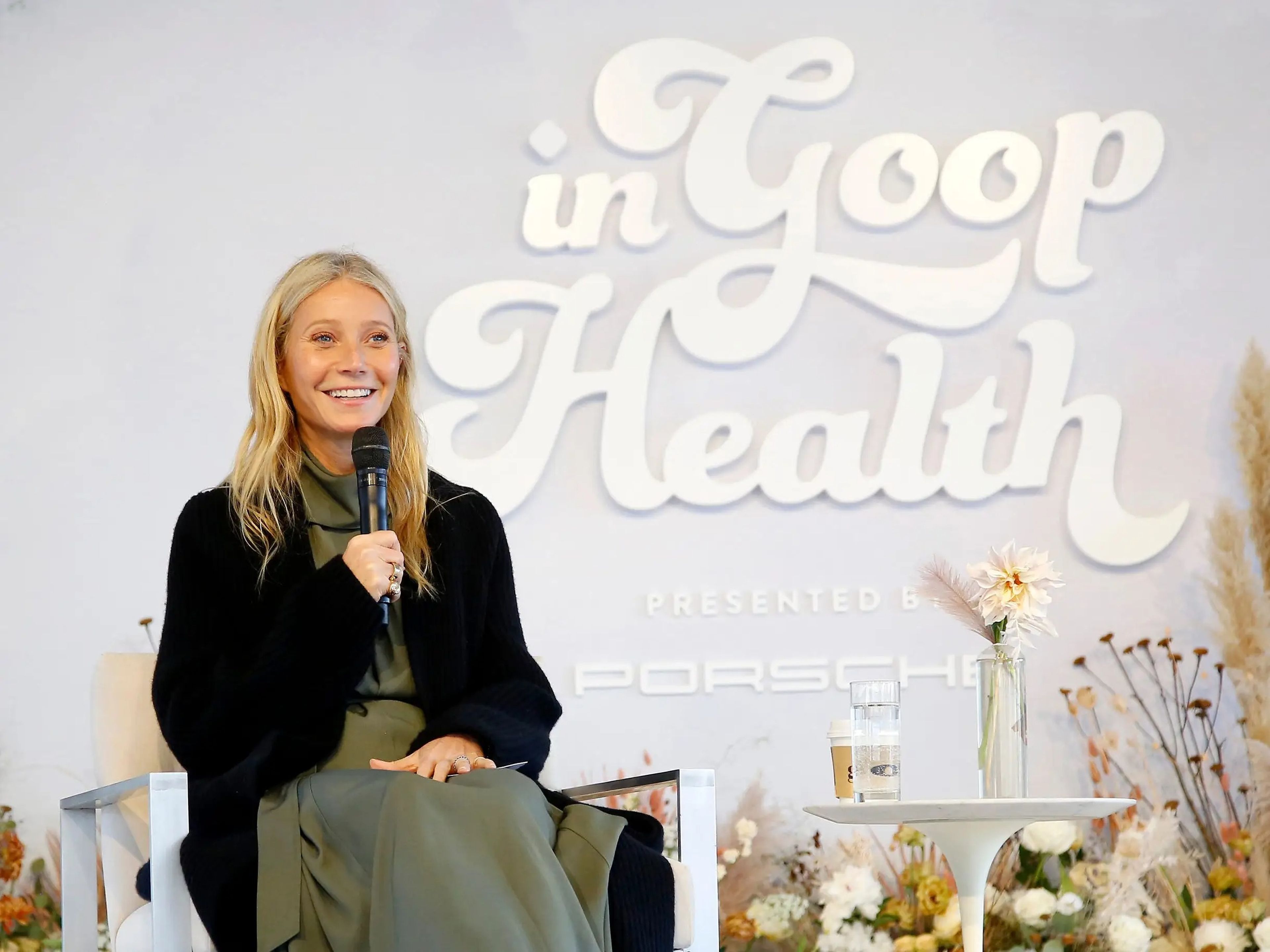 Paltrow sitting onstage with a microphone wearing a black sweater at a 'Goop in Health' event