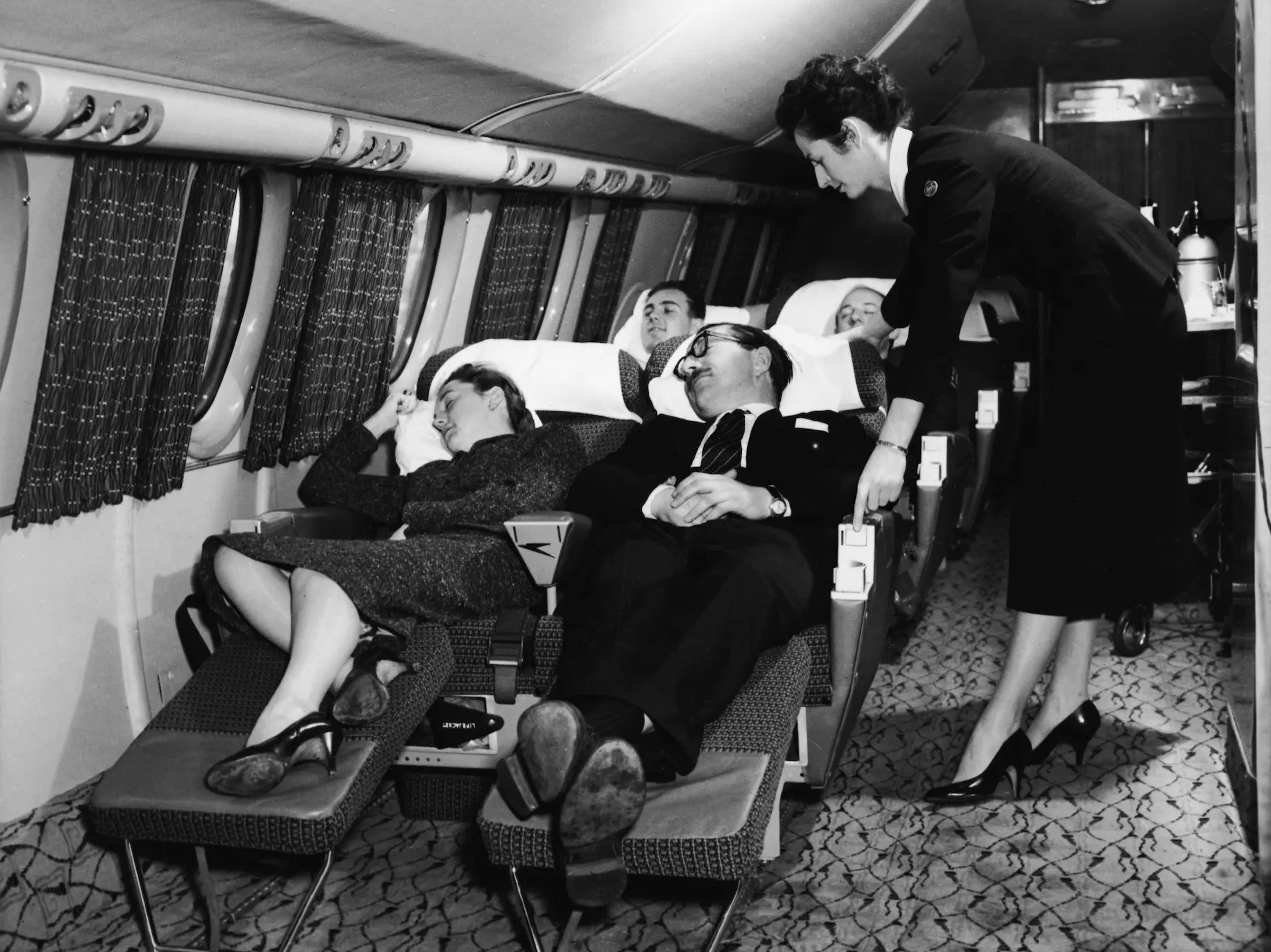 Passengers sleeping on recliners with a flight attendant assisting in the 1950s.