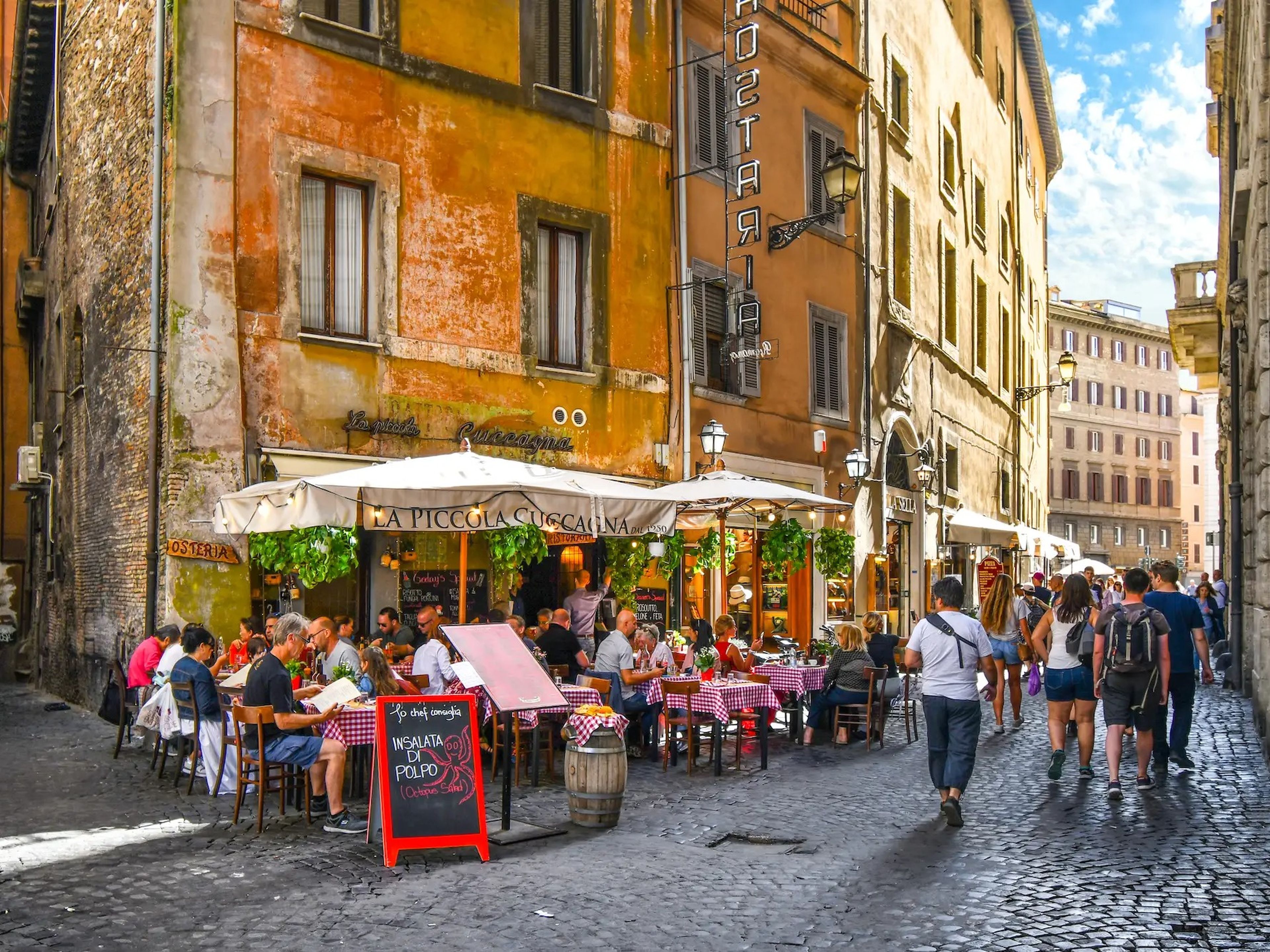 people dining outdoors at an italian restaurant in rome while others pass by on the cobblestone street
