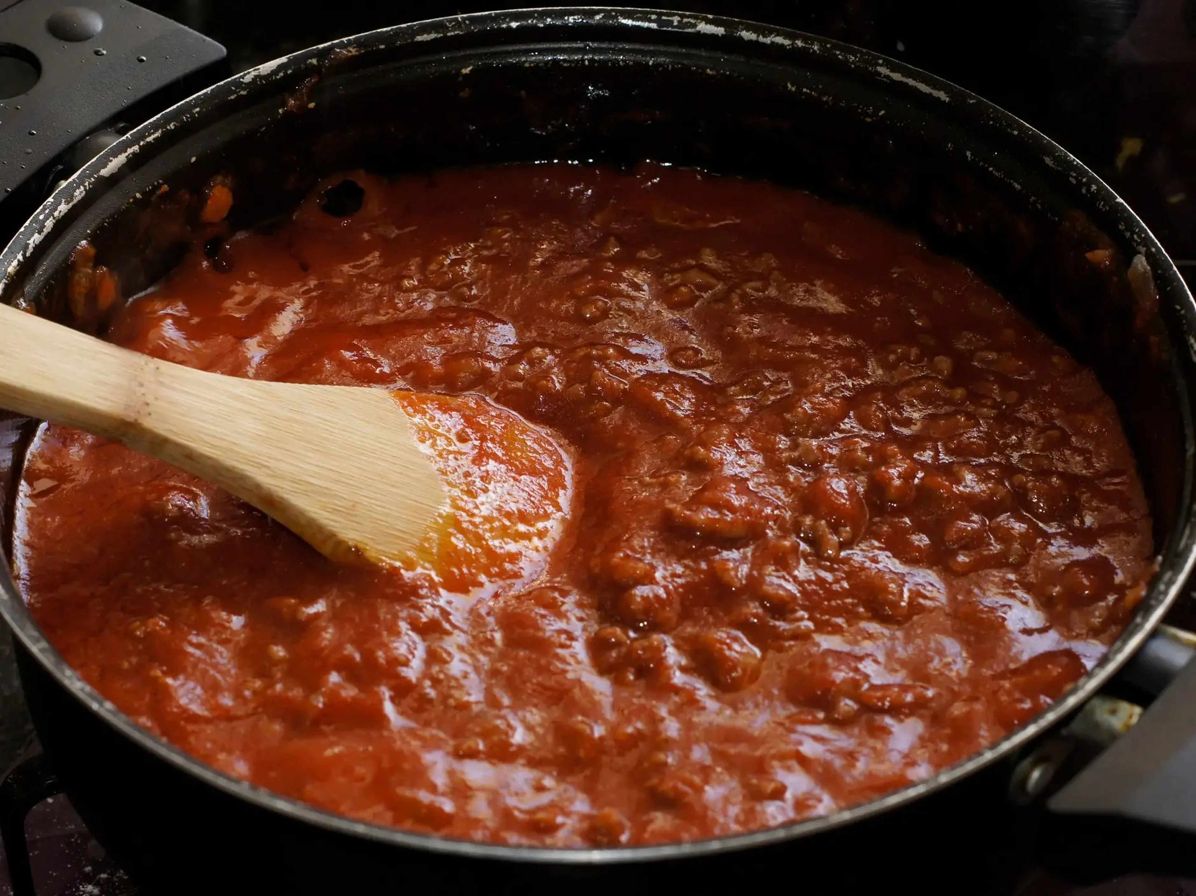 pot of red sauce stirred with wooden spoon