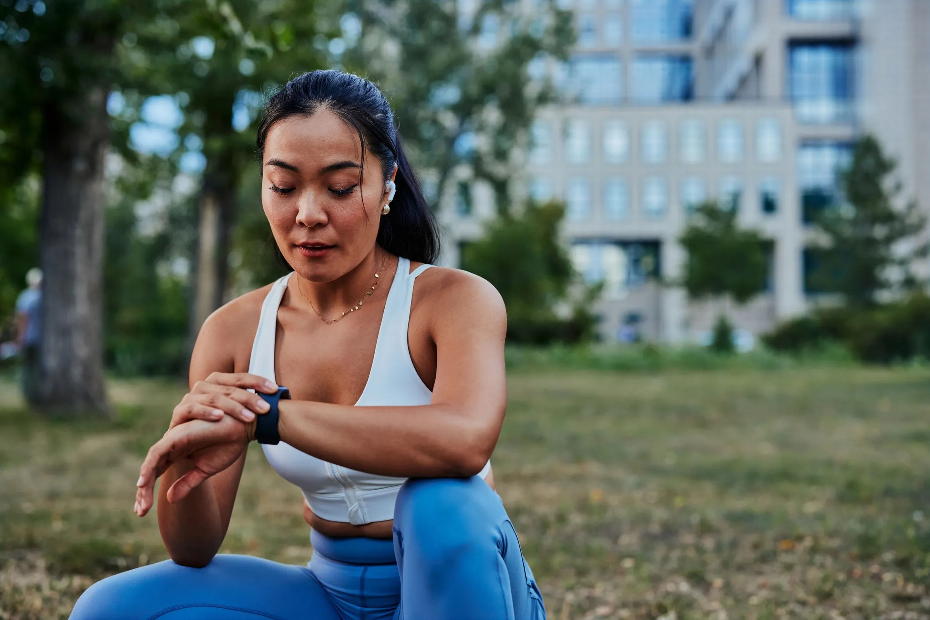 A woman in a sports bra and blue tights checking a smart watch on a run outside
