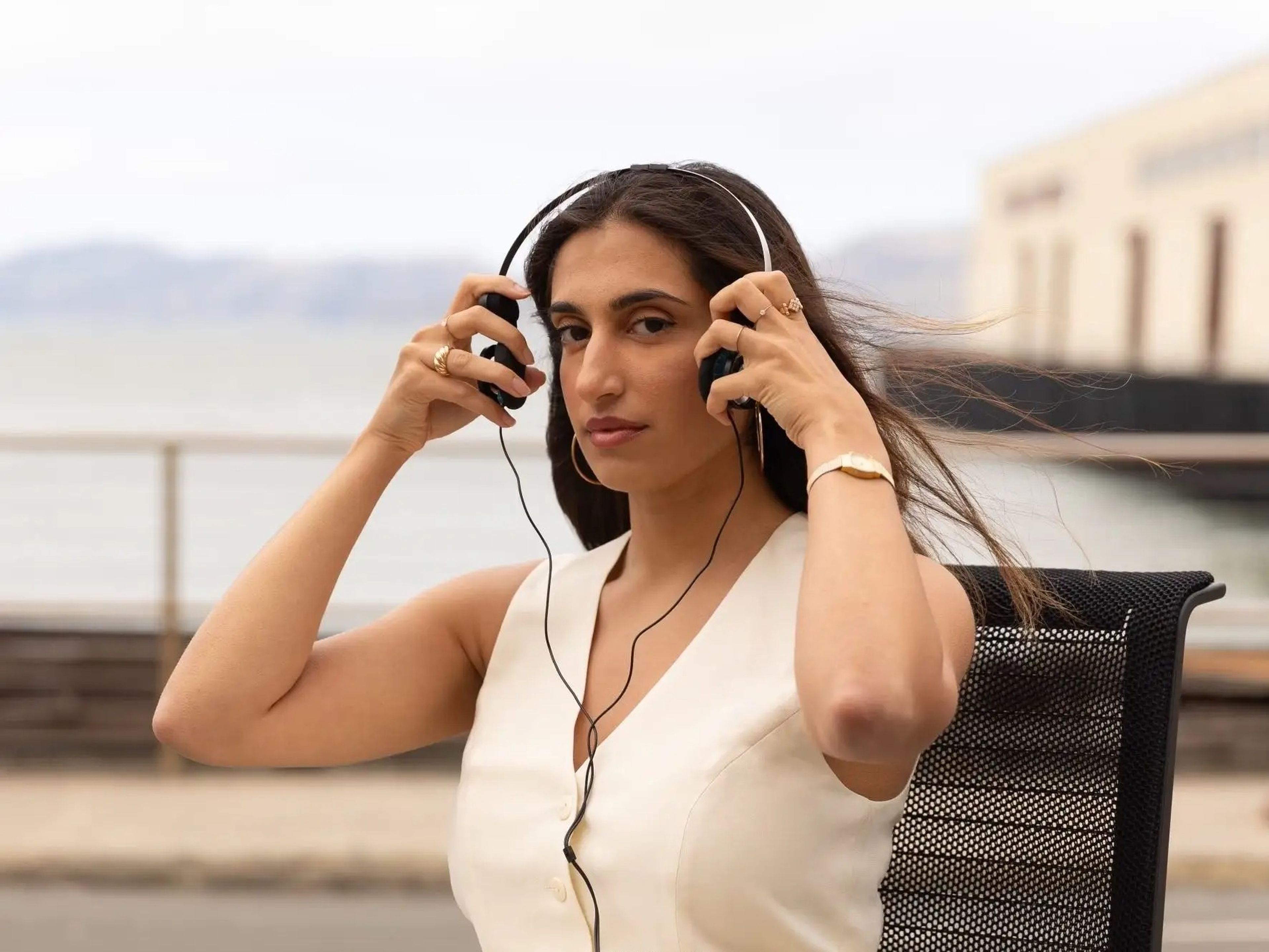 Avni Barman is wearing a white top while she looks at the camera and puts a pair of headphones on.