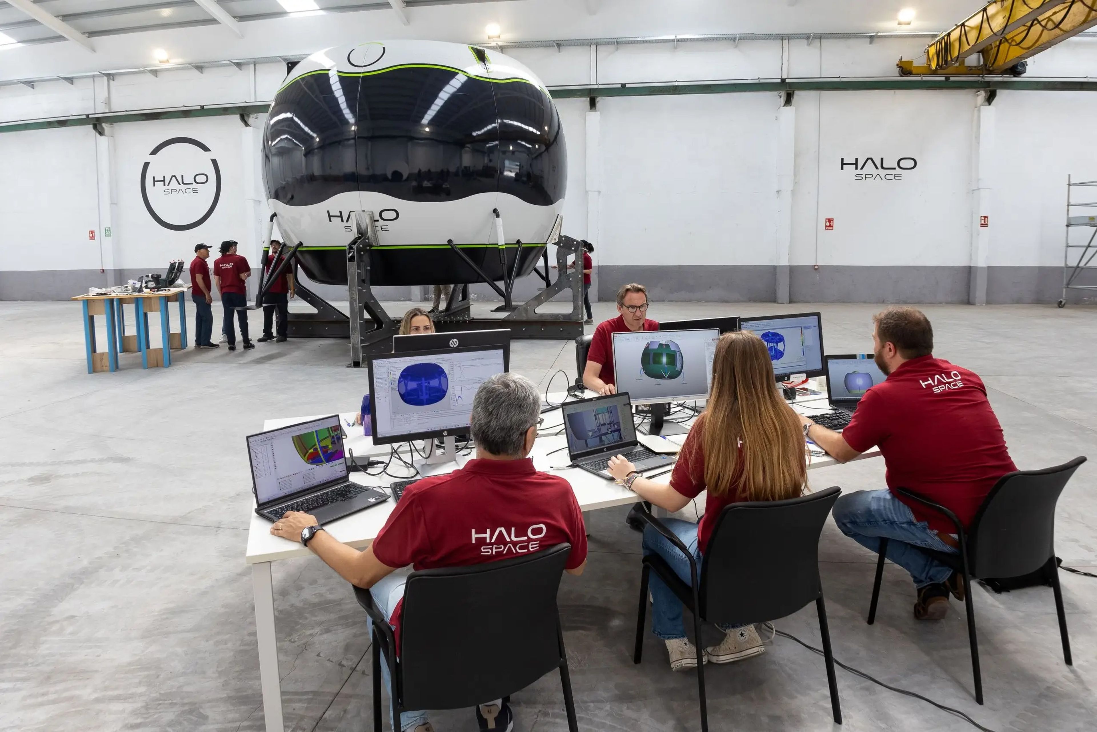 A Halo Space capsule in a hangar, and five employees sat at computers nearby wearing red shirts emblazoned with the company's name.