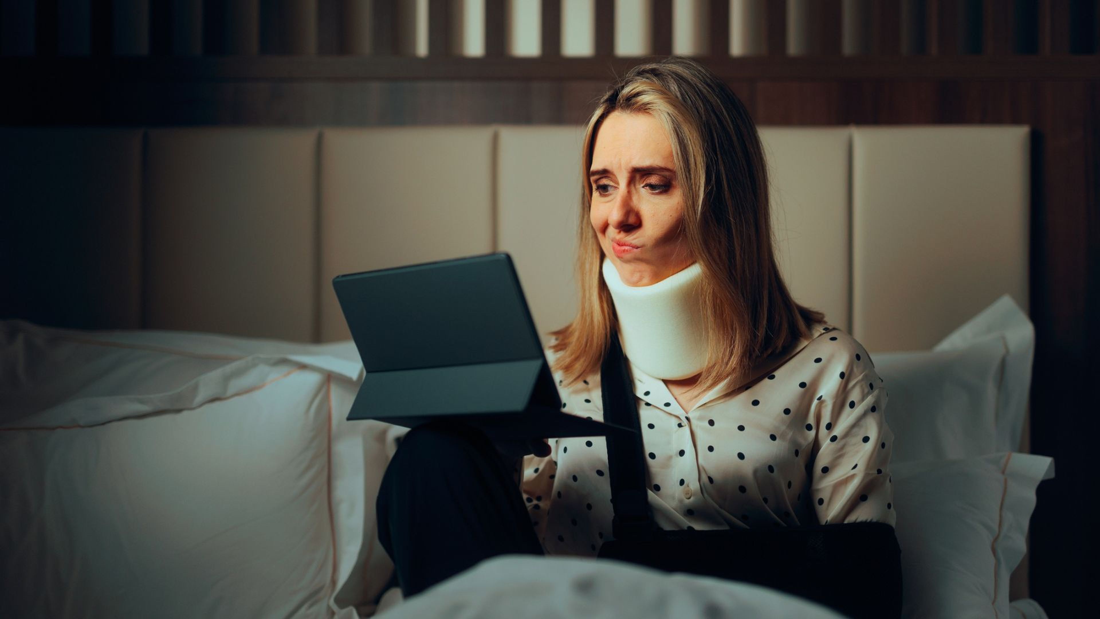 Una mujer con collarín pone una mueca mientras consulta su tablet.