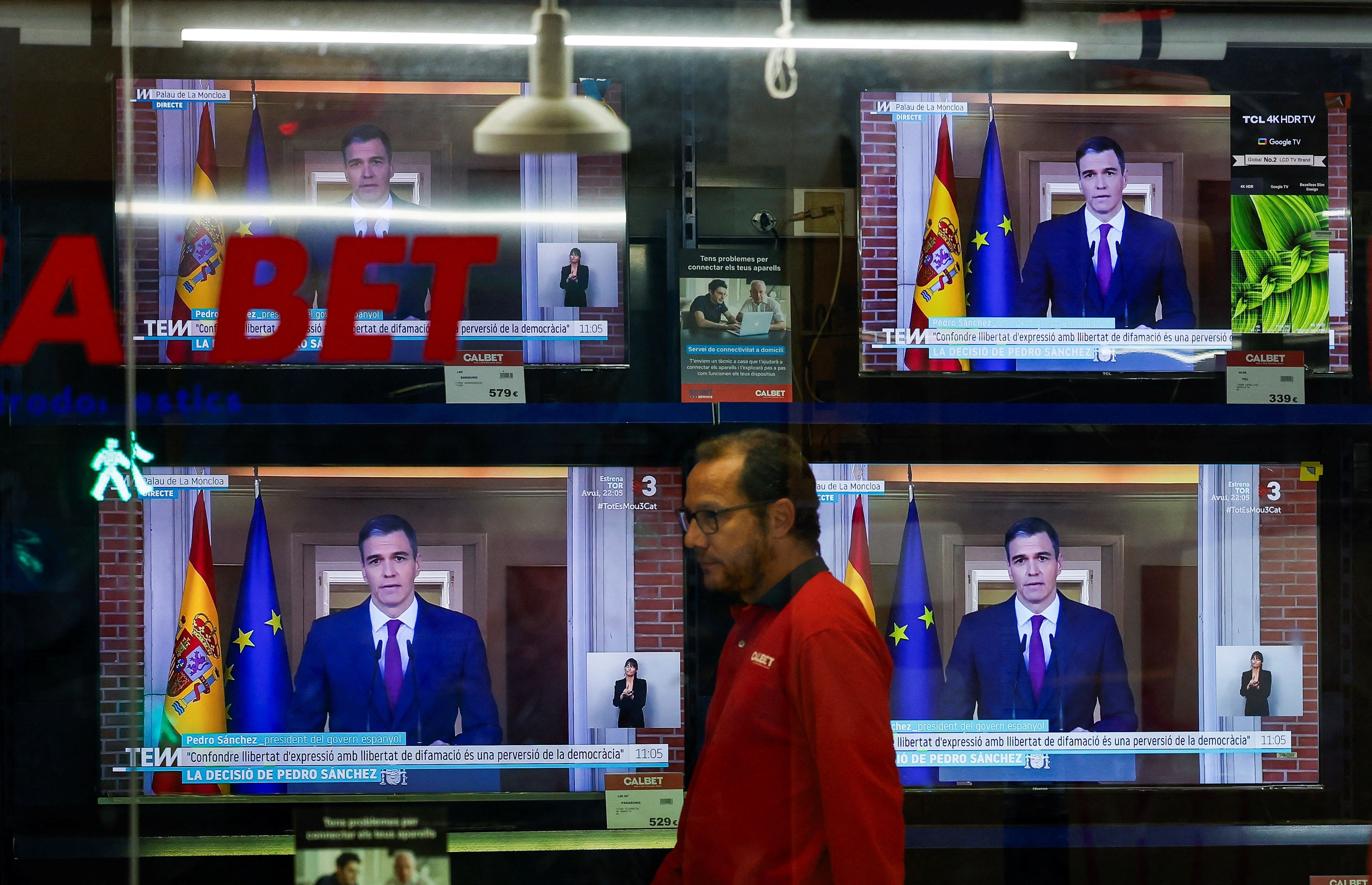 Un hombre pasea junto a un escaparate con varios televisores sintonizando el discurso de Pedro Sánchez.