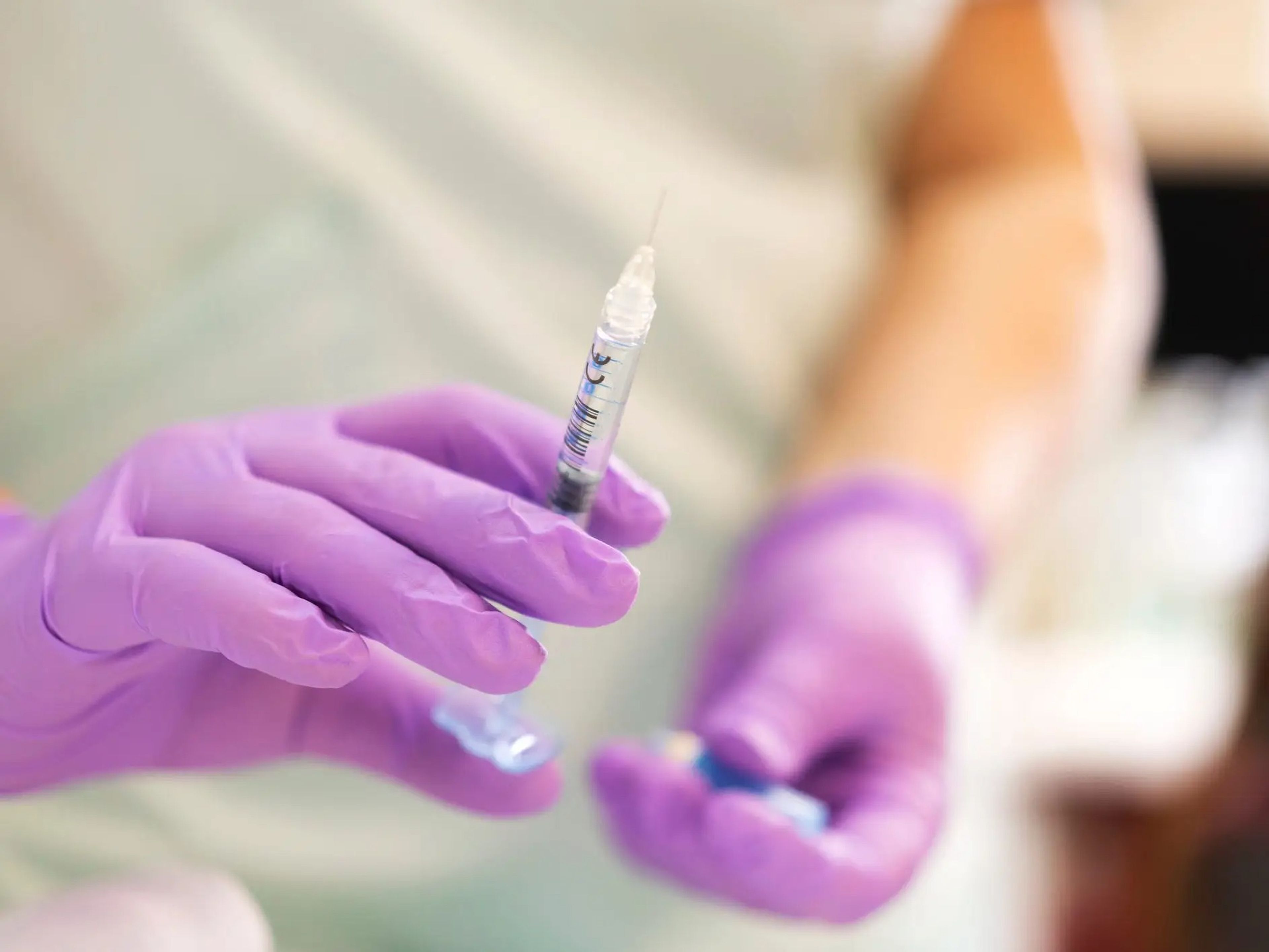 A person wearing purple plastic gloves and holding a syringe.