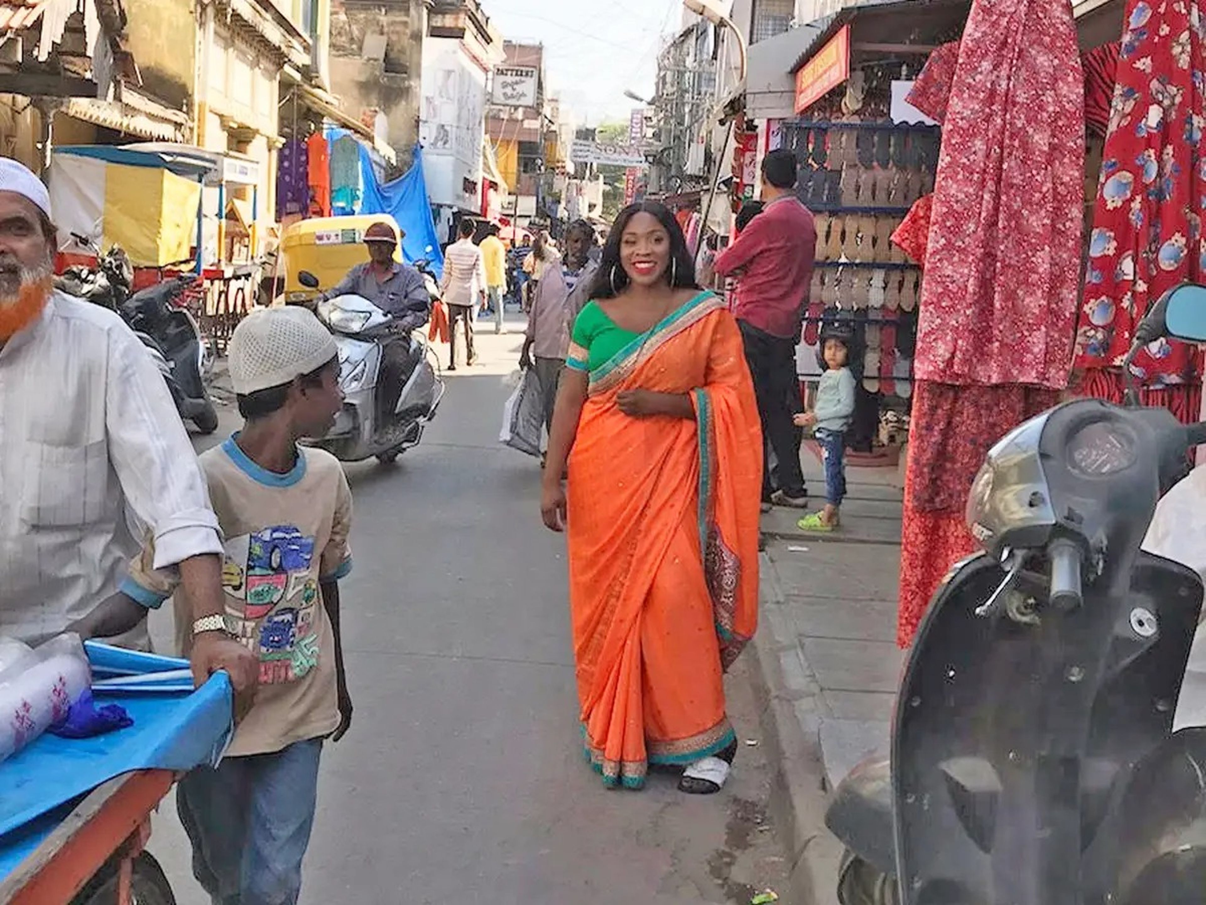 Photo of the writer in an orange sari and green shirt at a market full of vendors