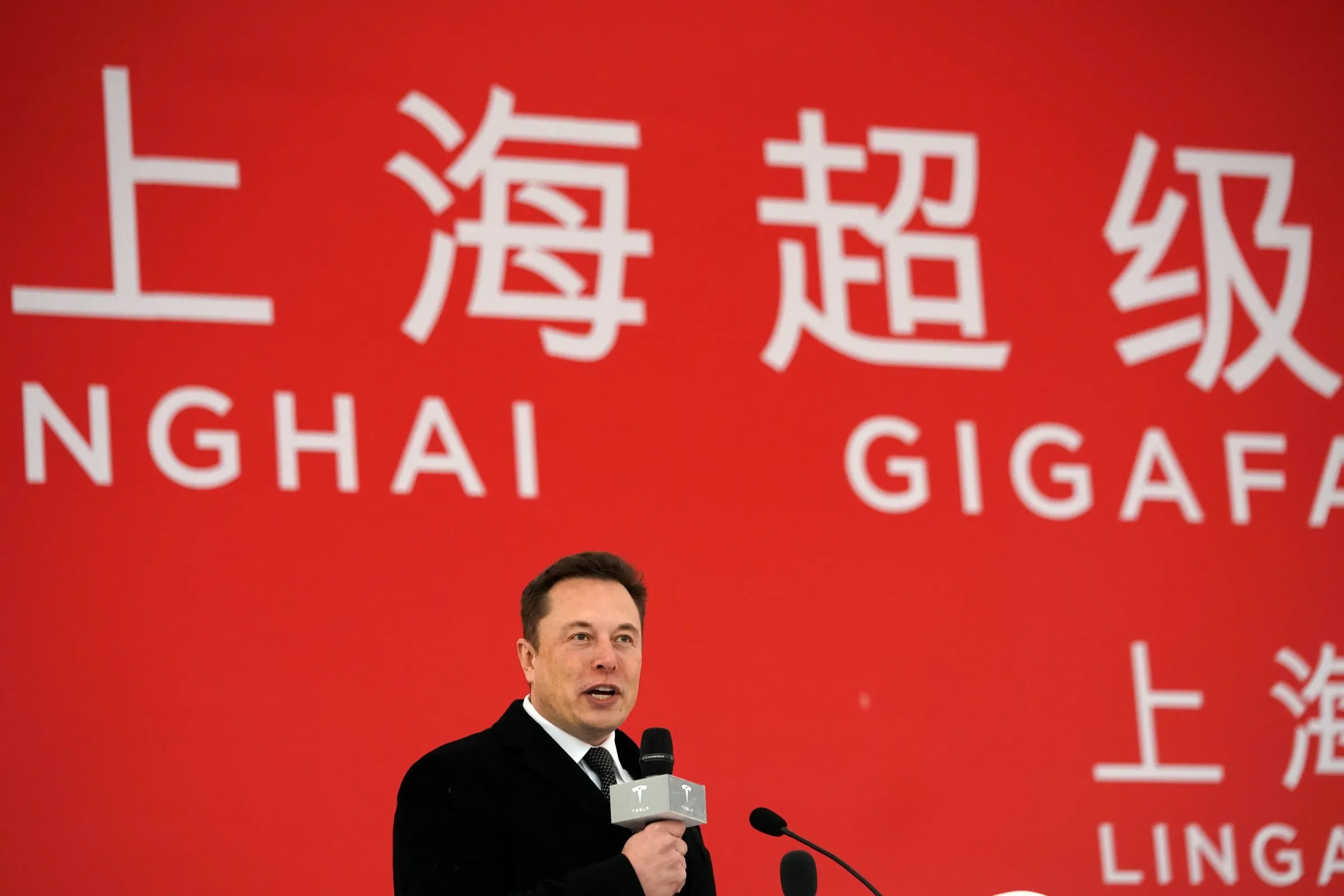 El CEO de Tesla, Elon Musk, asiste a la ceremonia de colocación de la primera piedra de la Gigafábrica de Tesla en Shanghái, China, el 7 de enero de 2019, sosteniendo un micrófono frente a una gran pancarta roja.