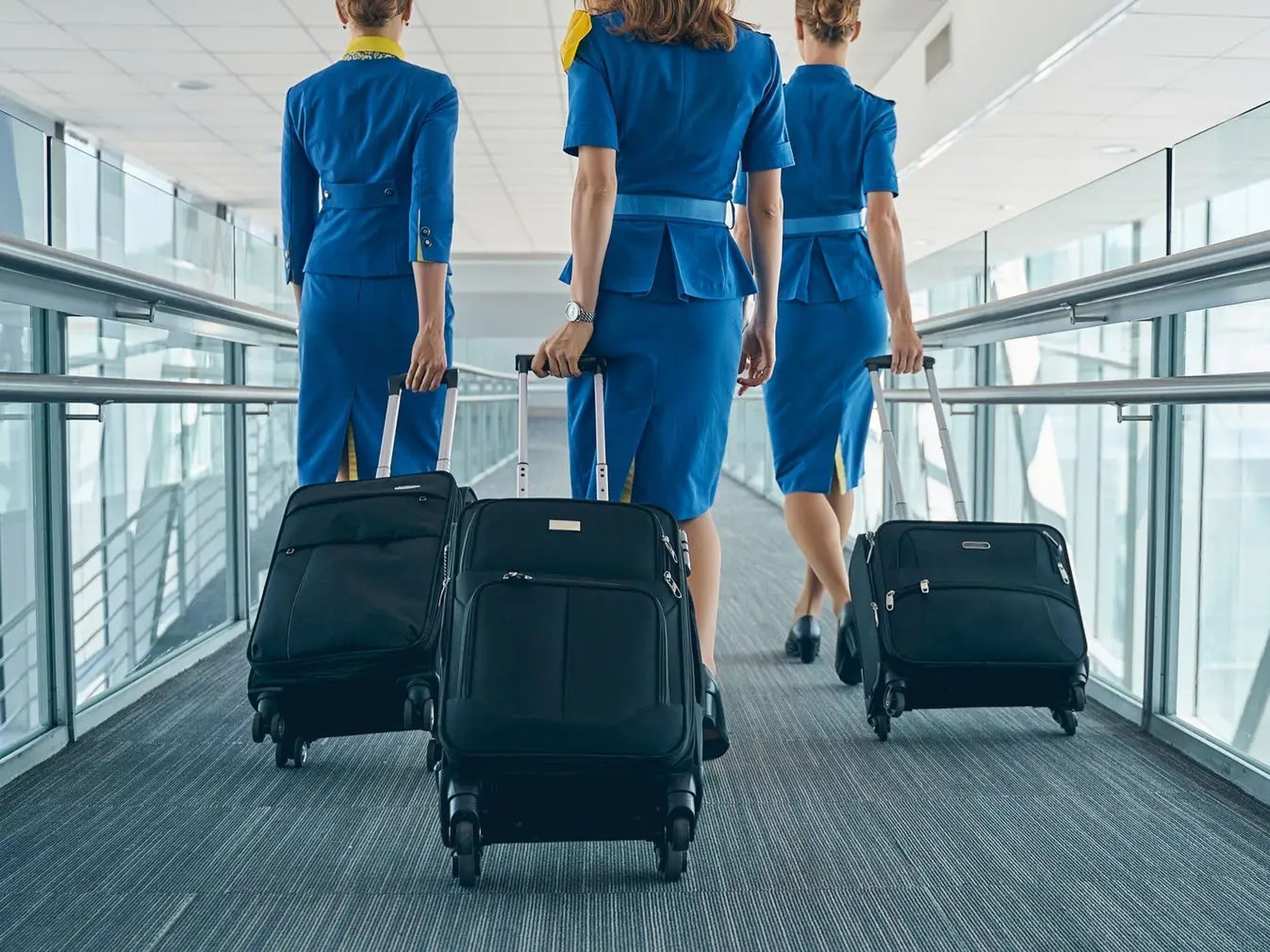 Three stewardesses in blue skirts and shirts with rolling suitcases behind them at an airport