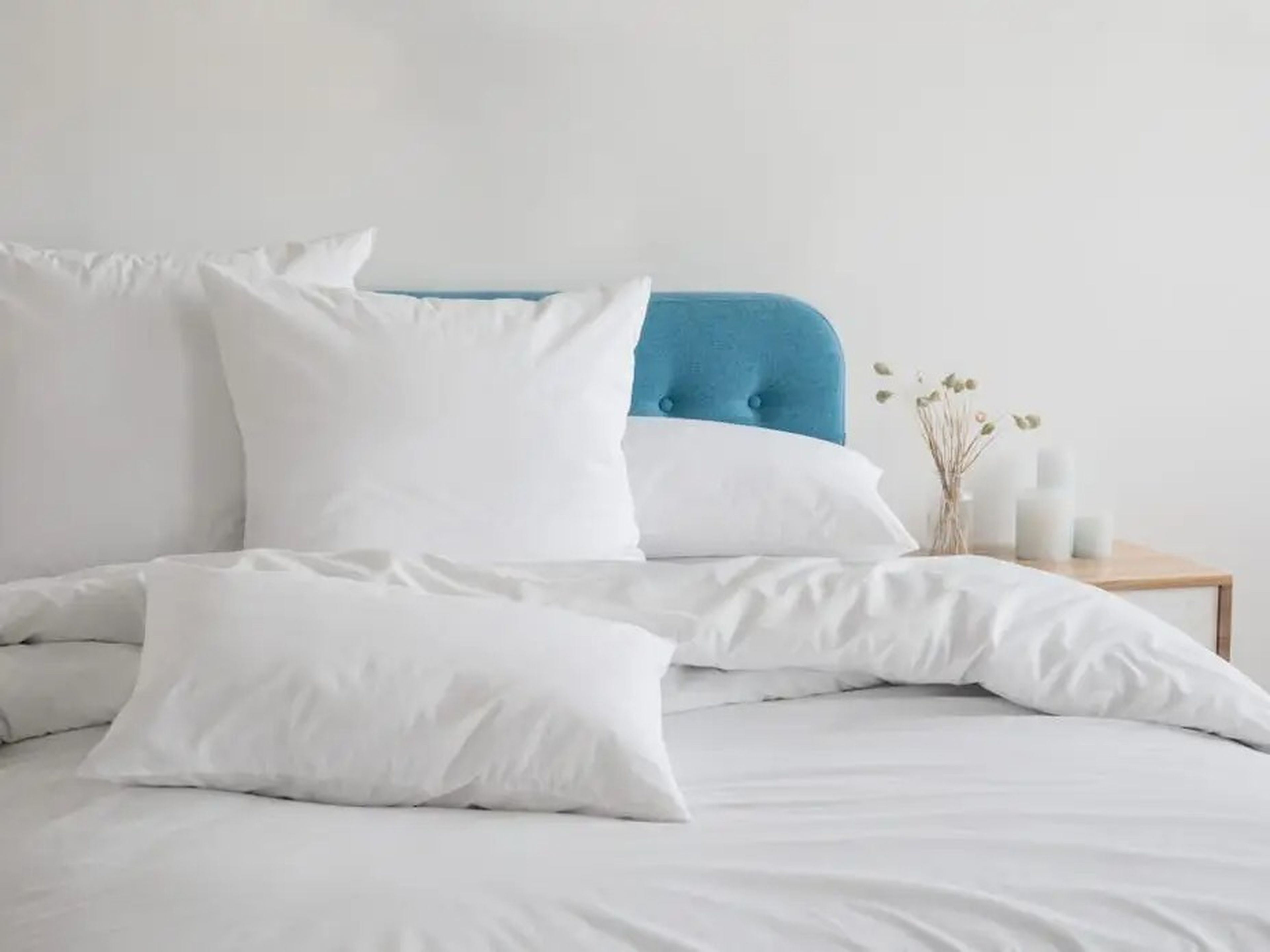 Almohadas, edredón y funda nórdica blancos sobre una cama azul.