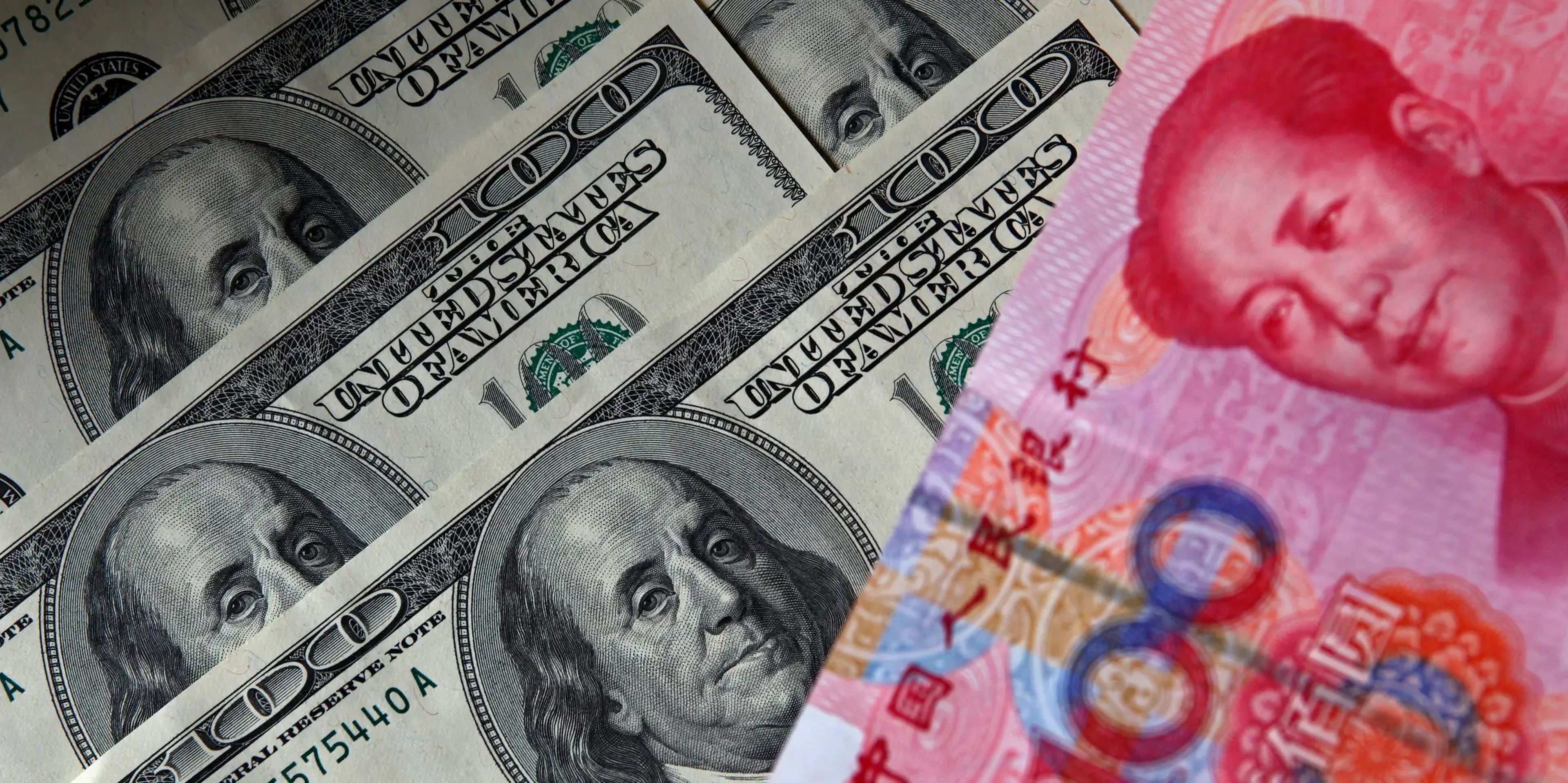 Un billete de 100 yuanes junto a varios billetes de 100 dólares. 