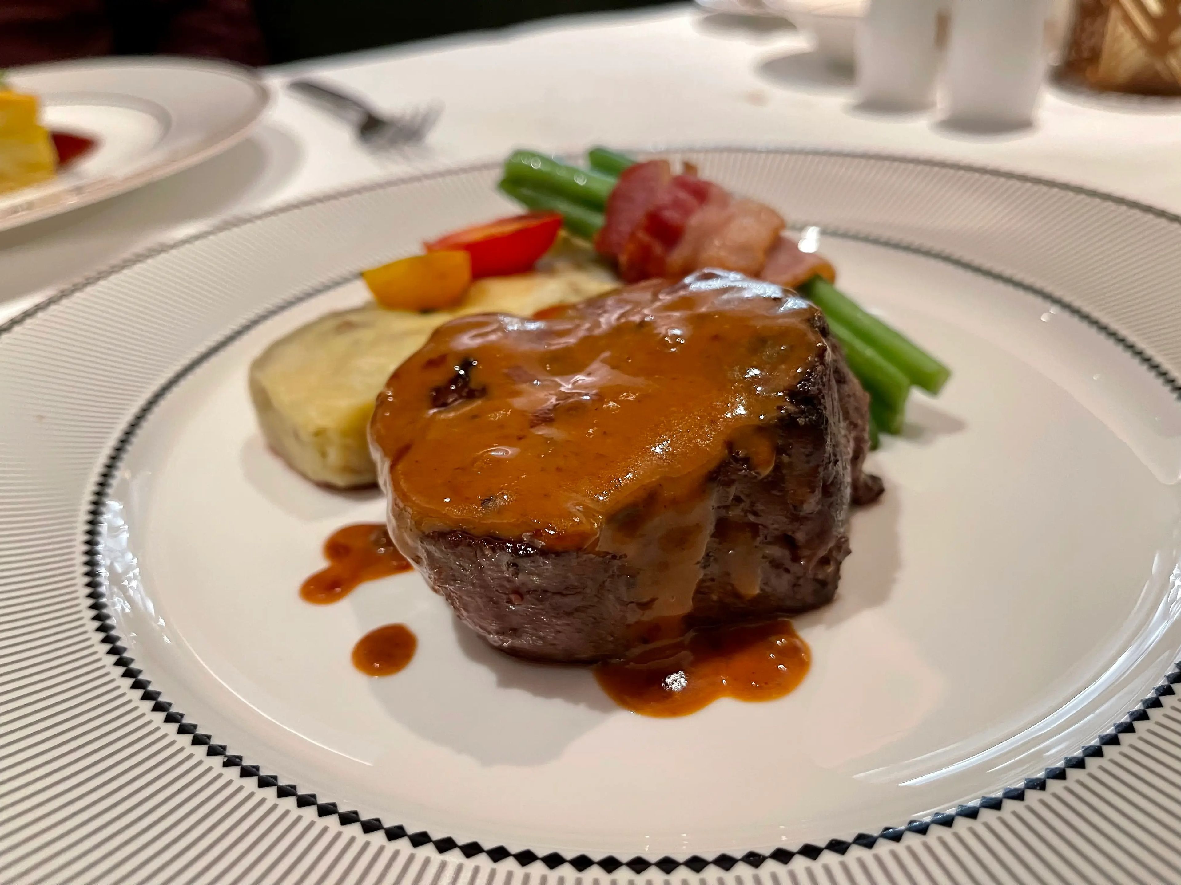 A piece of steak with gravy and vegetables on a plate.