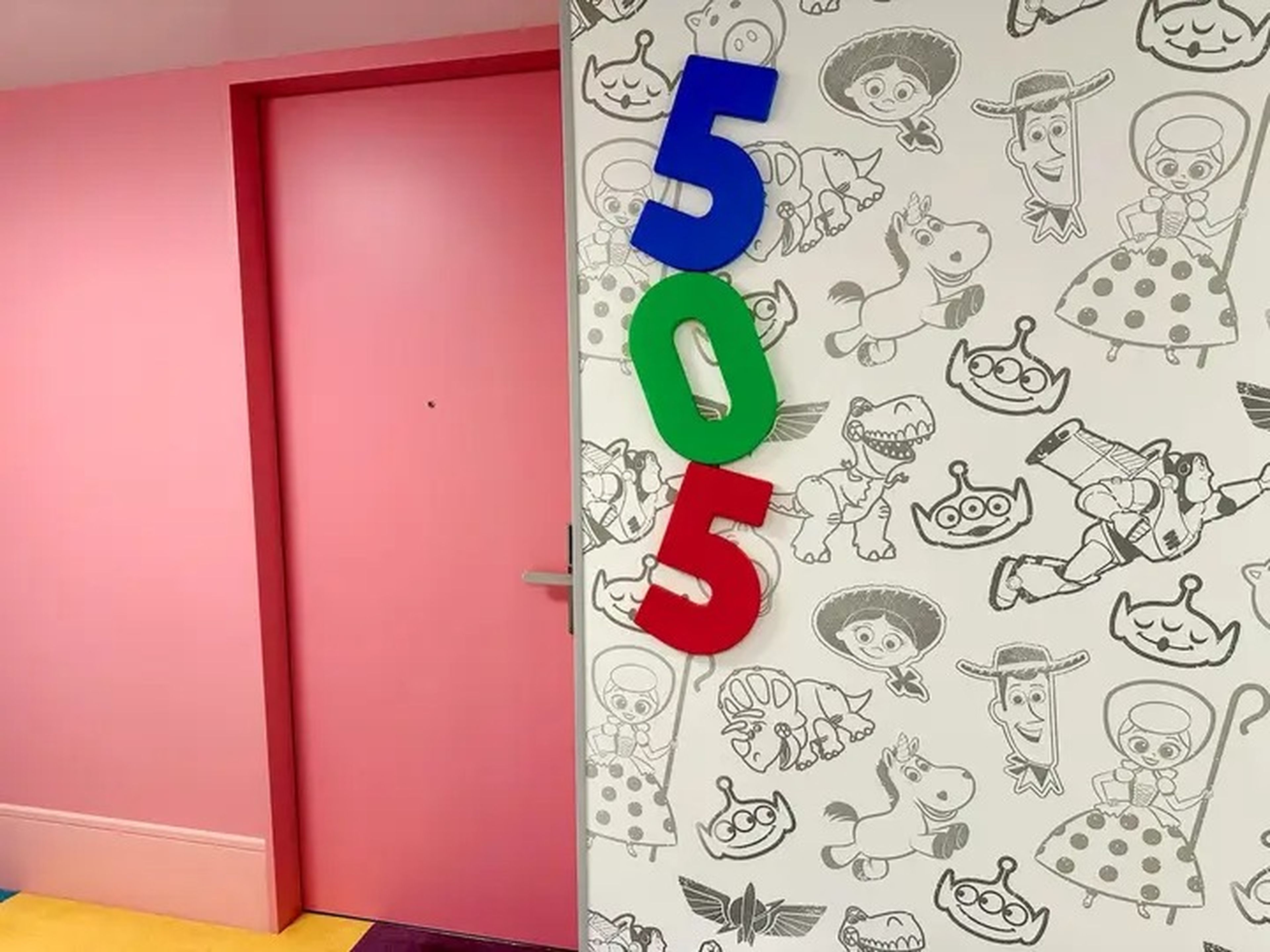 A room entrance at the Tokyo Toy Story Hotel shows a colorful pink door that is lined with the numbers 505 in blue, green, and red.