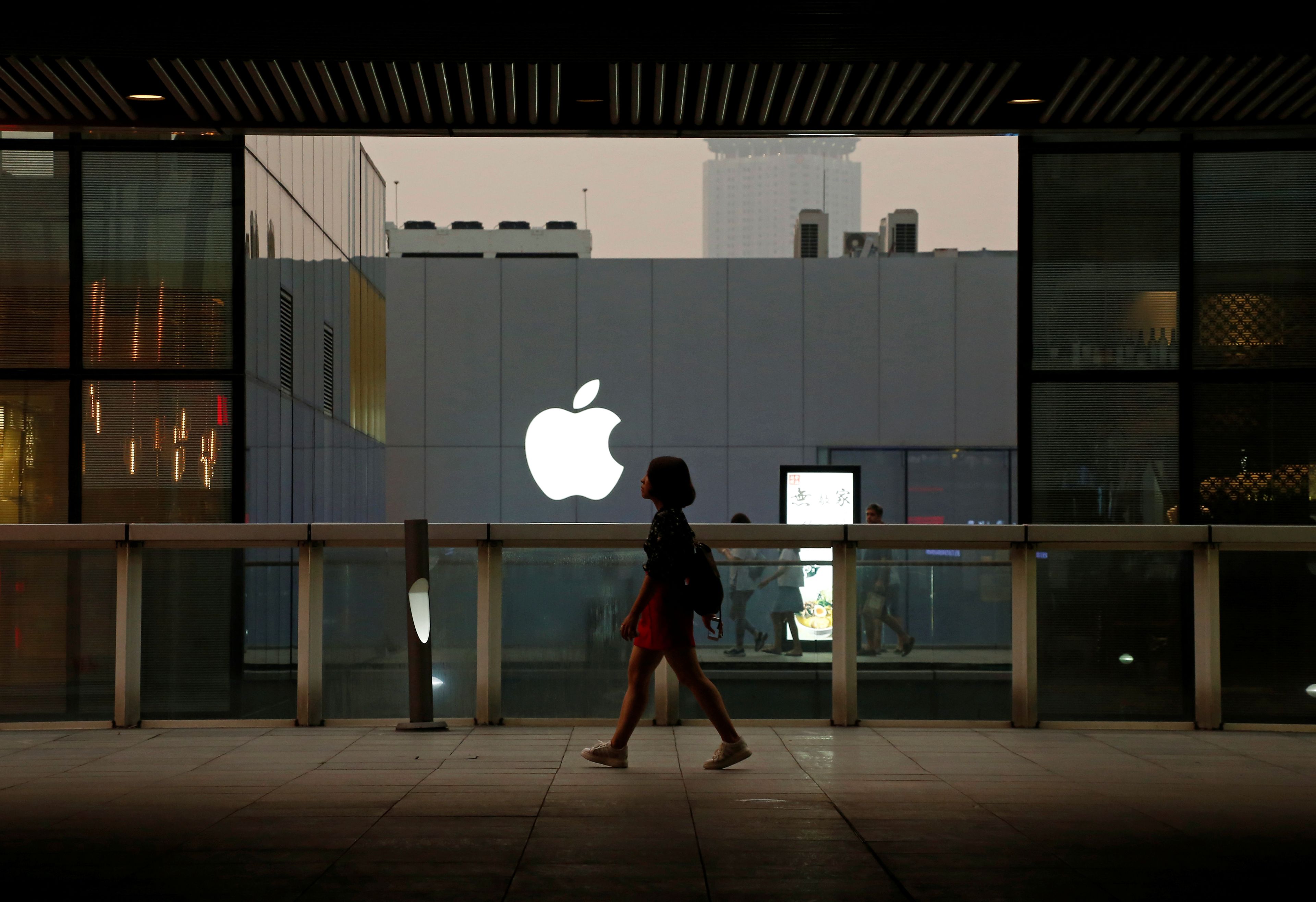 Una mujer andando con el logo de Apple detrás